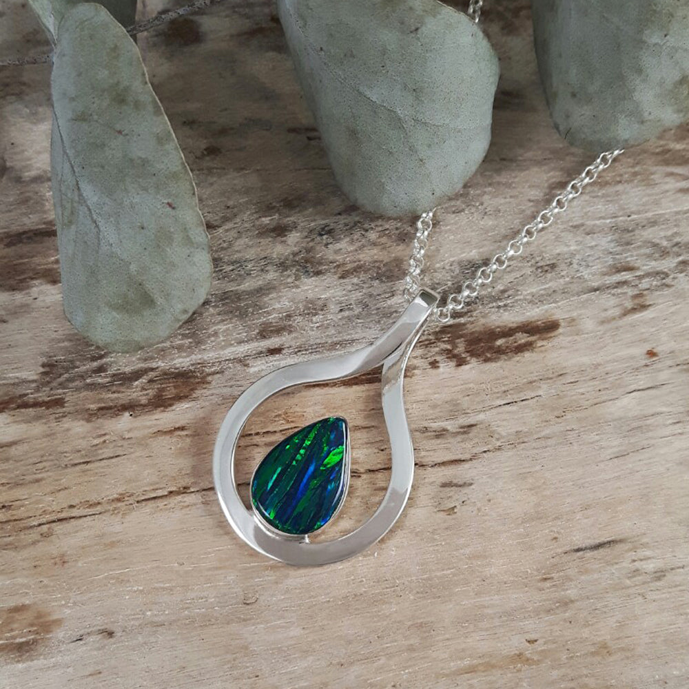 A sterling silver pendant with an emerald cultured opal teardrop centerpiece, displayed on a wooden surface.