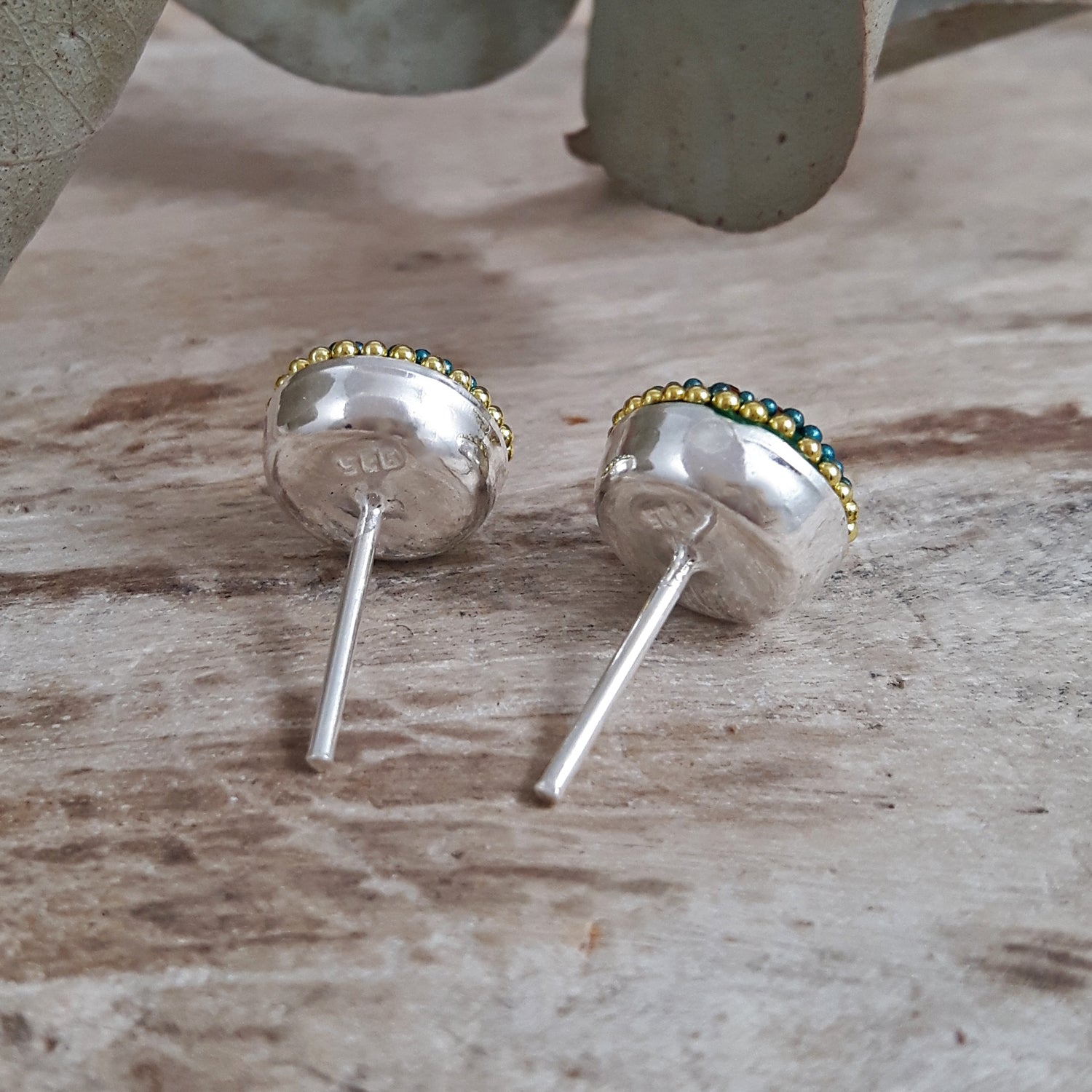 Sterling silver stud earrings with green and gold accents on a wooden surface