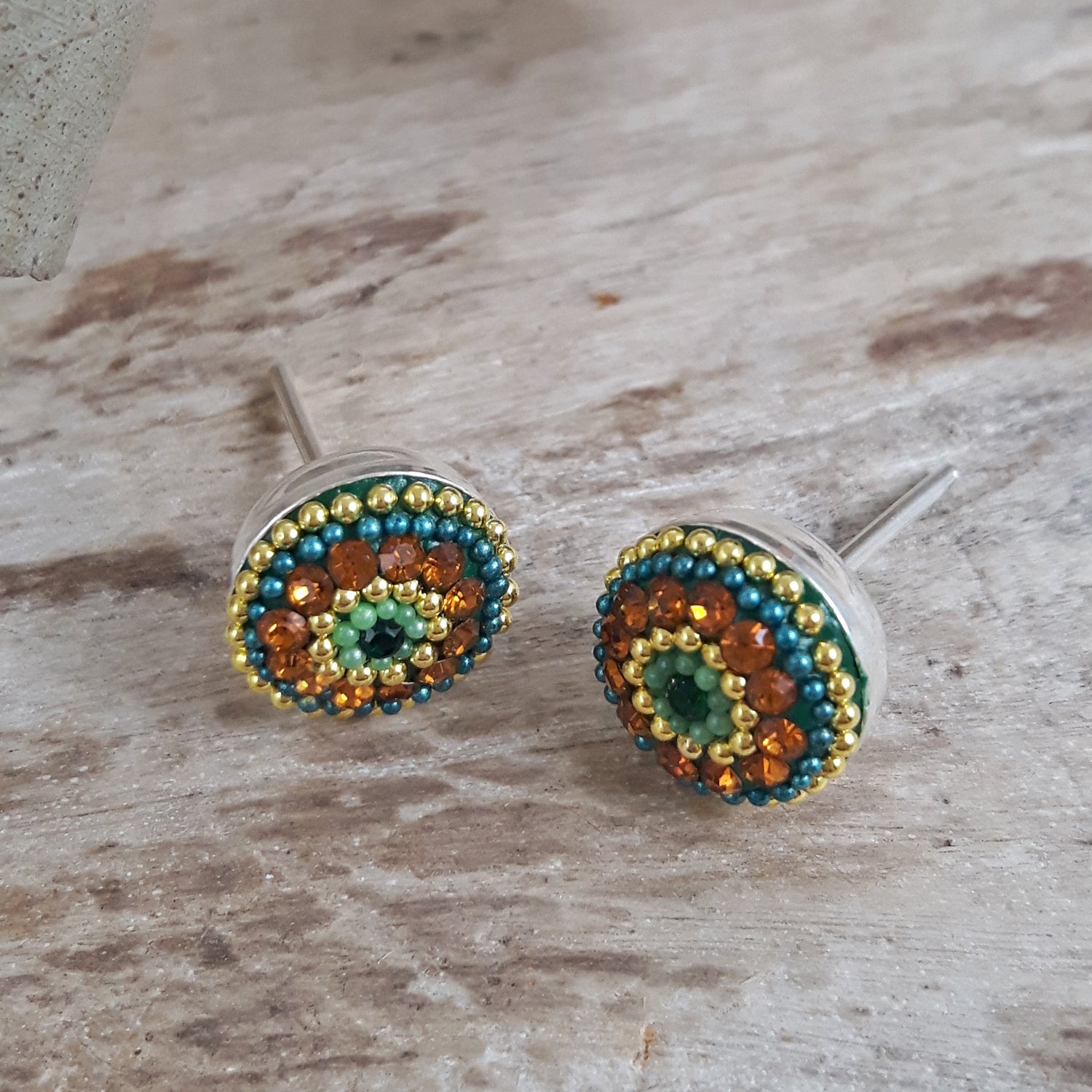 Pair of hand-applied micro-bead and crystal stud earrings on a wooden surface