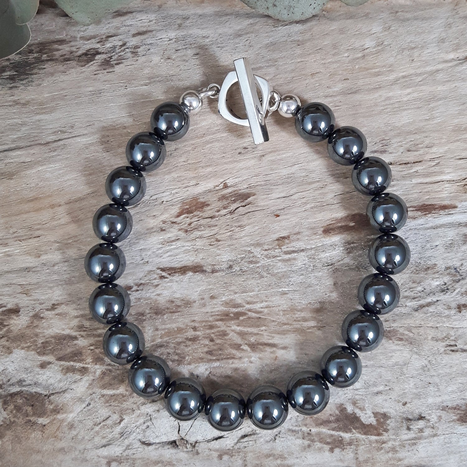 Black beaded hematite bracelet with a sterling silver t-abr on a wooden surface, artisan jewellery