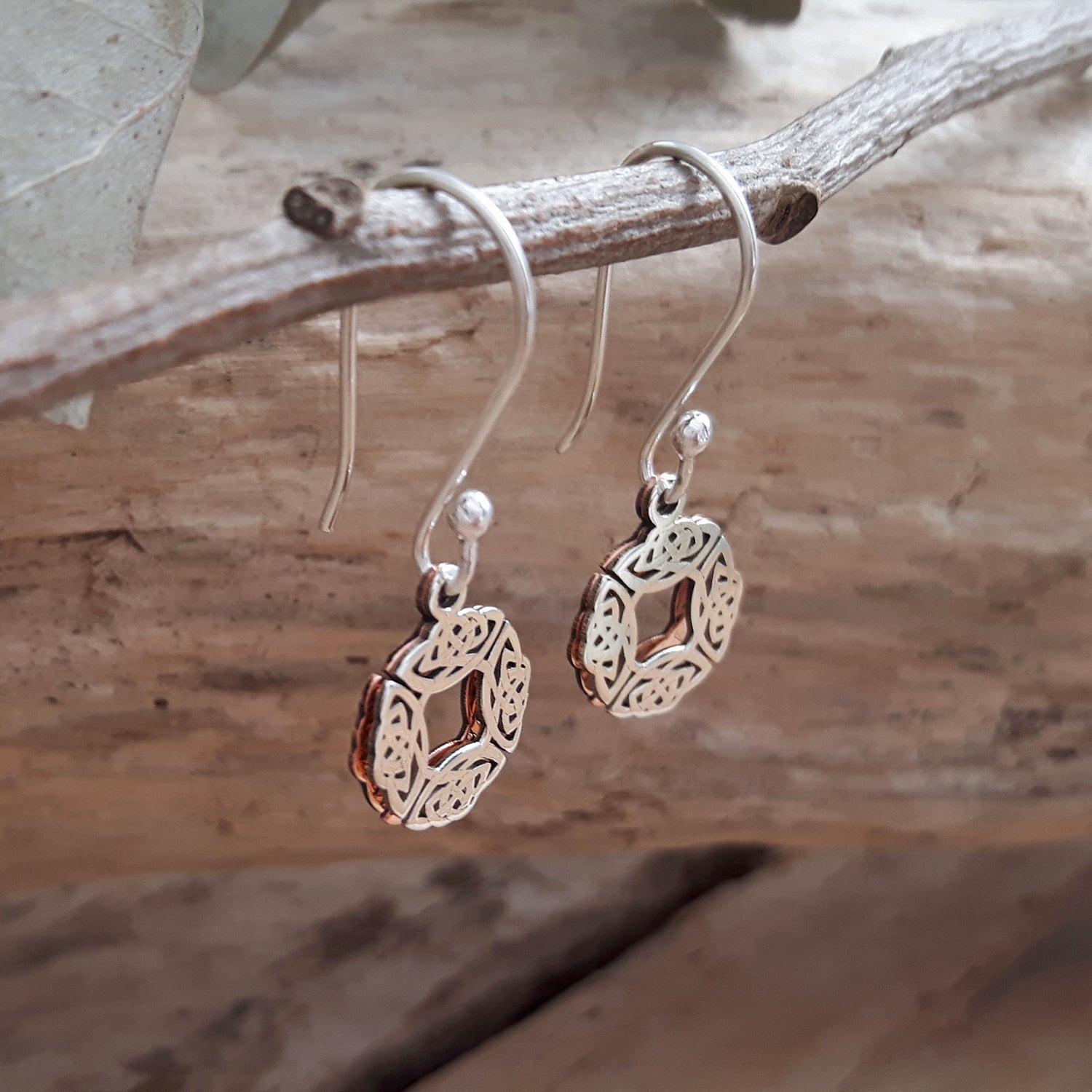 Sterling silver & copper drop earrings with intricate designs hanging on a branch.