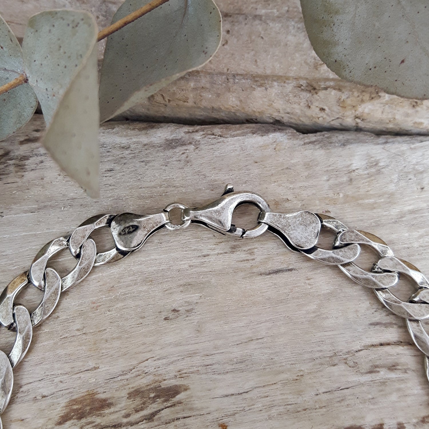 Oxidised sterling silver chain bracelet on a wooden surface with leaves in the background