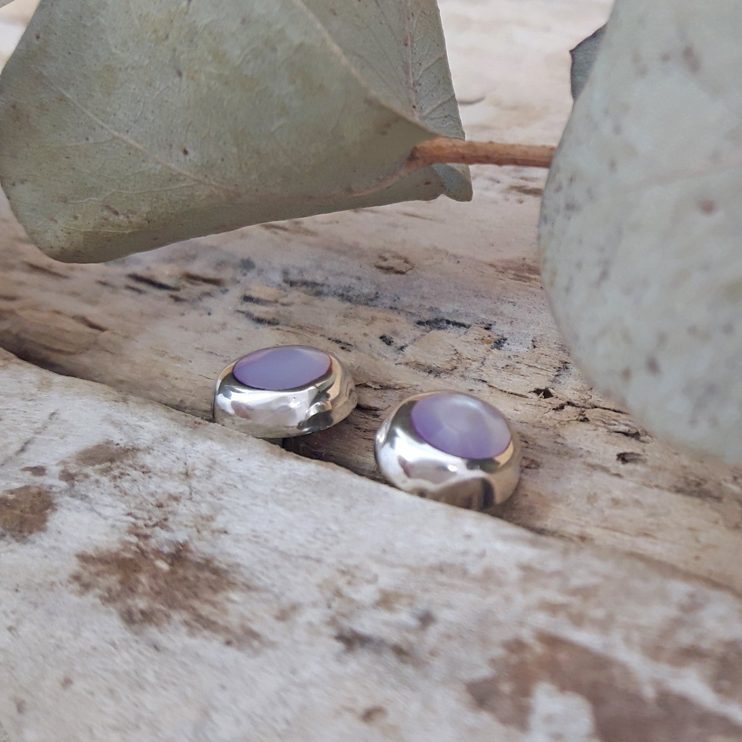Close-up of pink mother-of-pearl circle stud earrings in 925 sterling silver nestled in driftwood, soft blush shell detail.