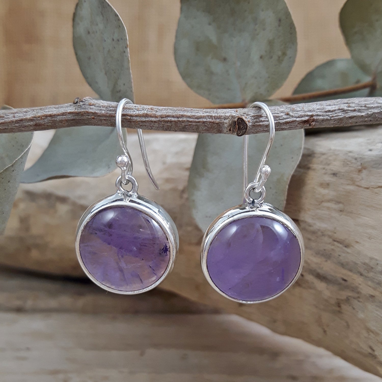 Purple amethyst gemstone earrings with sterling silver rims on a branch with leaves in the background