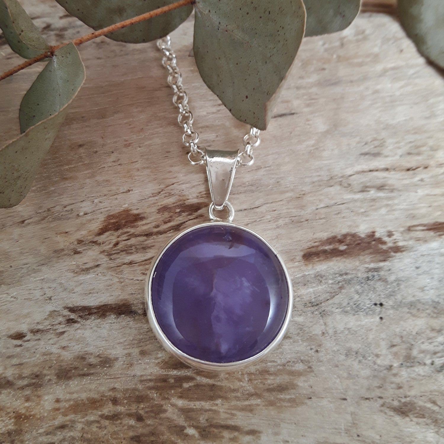 Purple amethyst gemstone pendant photographed on a sterling silver chain on a wooden surface with leaves in the background