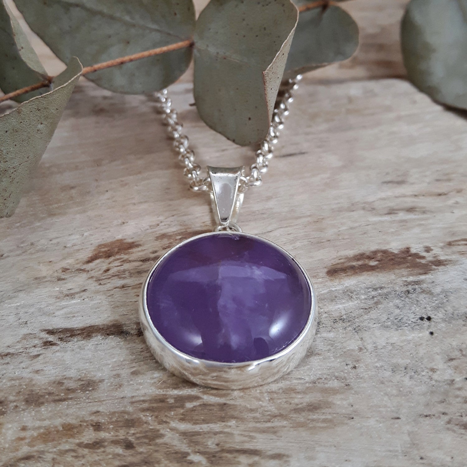 Purple amethyst pendant on a sterling silver chain shown on a wooden surface with eucalyptus leaves