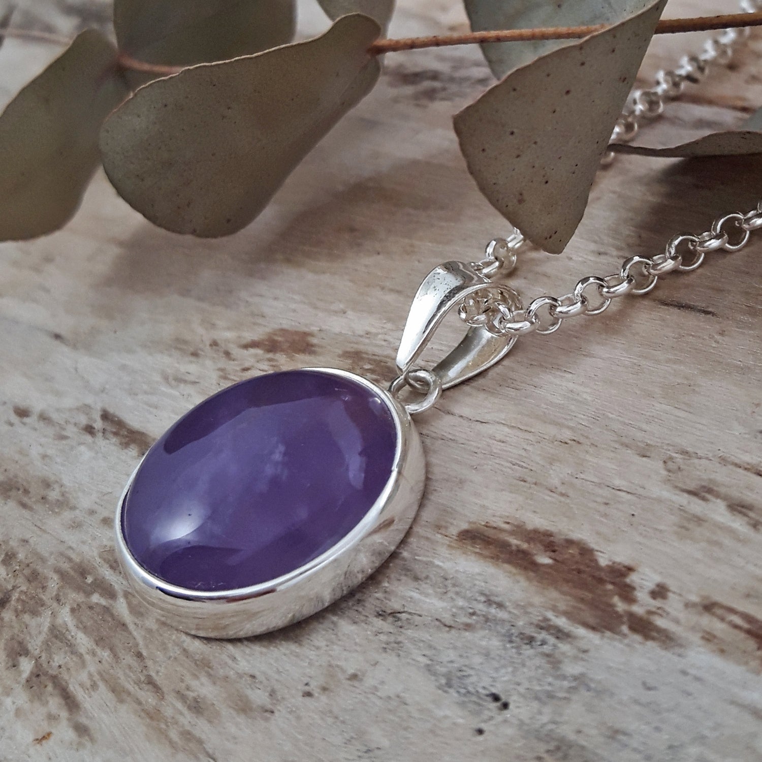 Sterling silver amethyst gemstone purple pendant on a wooden surface with leaves.