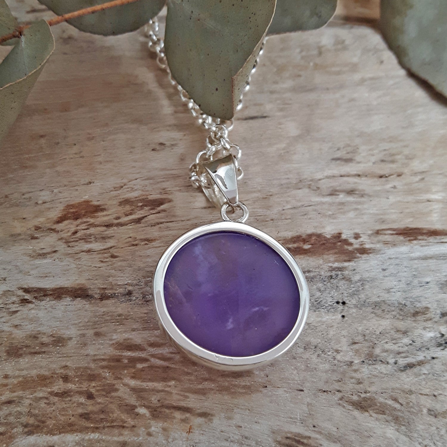 Purple amethyst pendant on a sterling silver chain against a wooden background