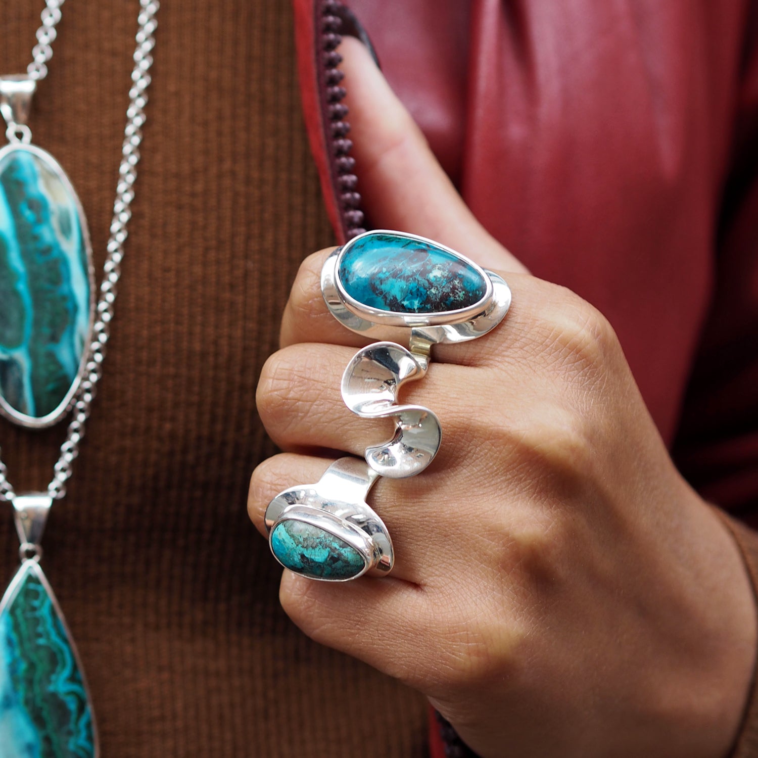 Hand wearing a polished sterling silver ring with two shattakite gemstone rings, with additional jewellery in the background.