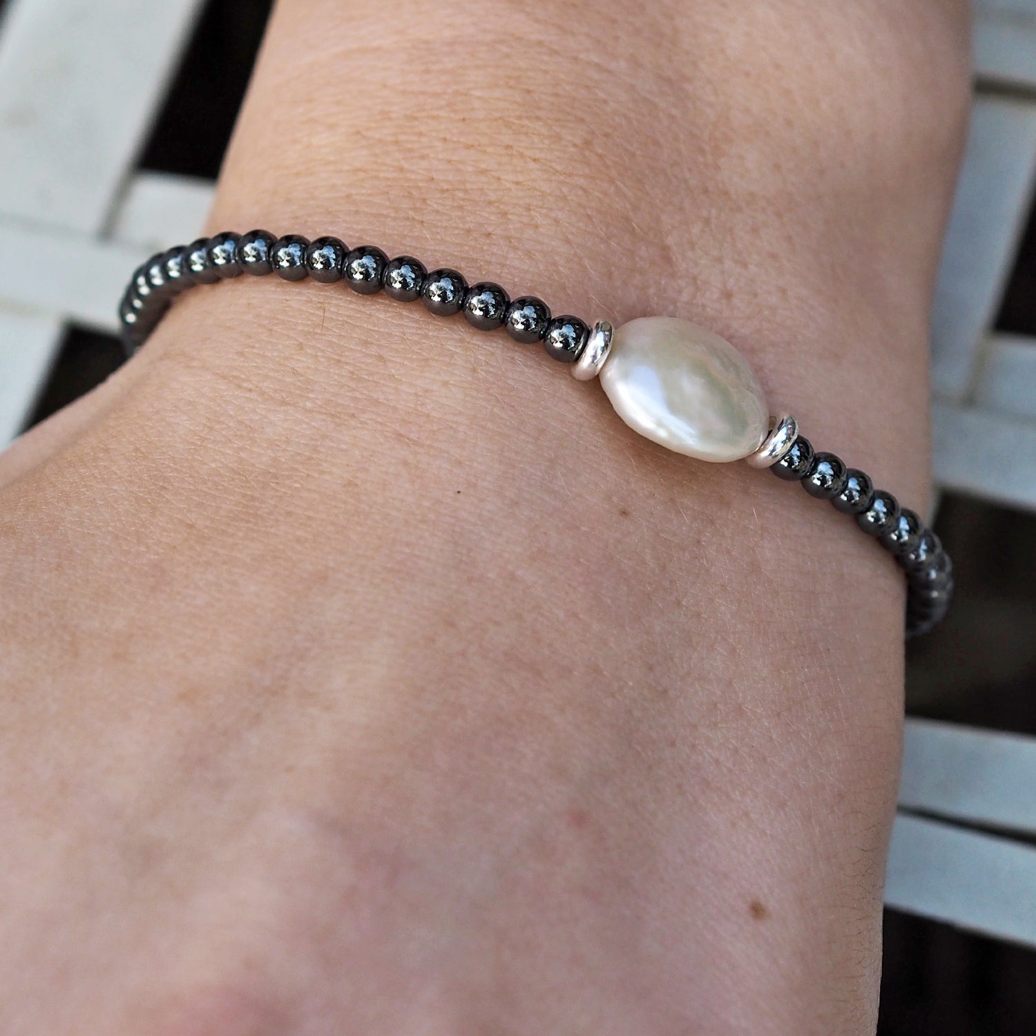 Handmade bracelet with hematite beads and a large pearl on the wrist against a blurred background