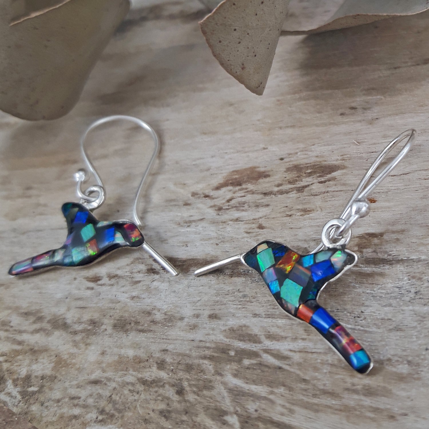 Colorful bird-shaped silver and opal earrings on a wooden surface