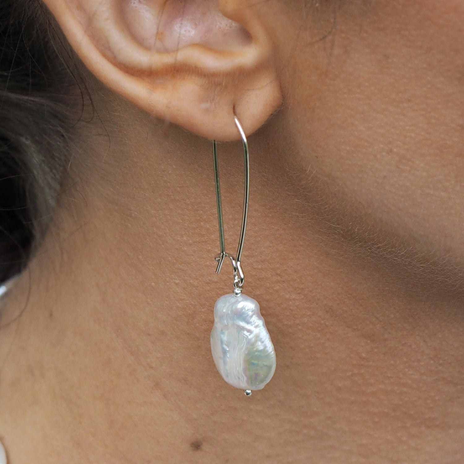 Baroque pearl earring worn by a person, with a close-up of the ear and skin. UK gifts under £40