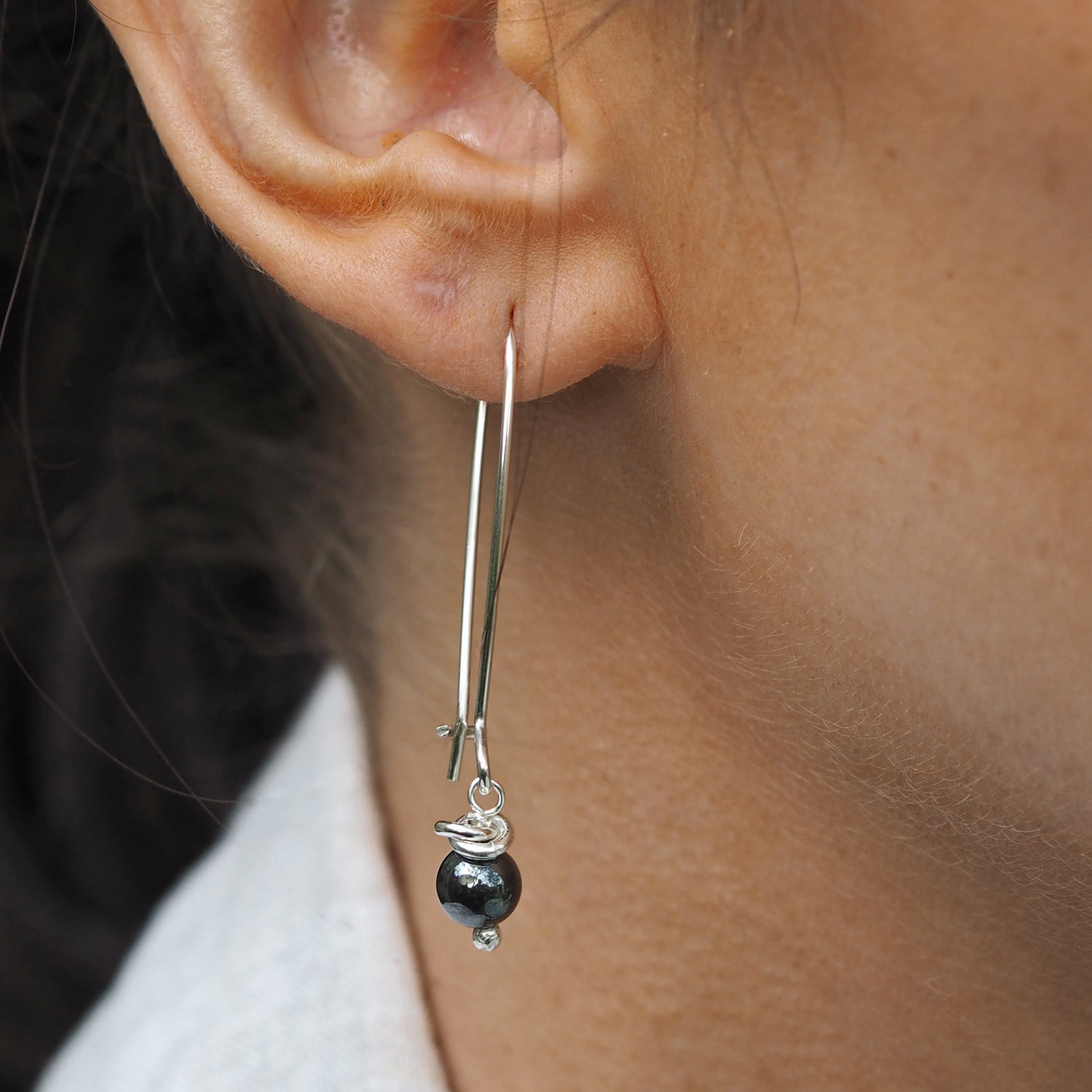 Close-up of an ear wearing a silver earring with a black hematite gemstone bead.
