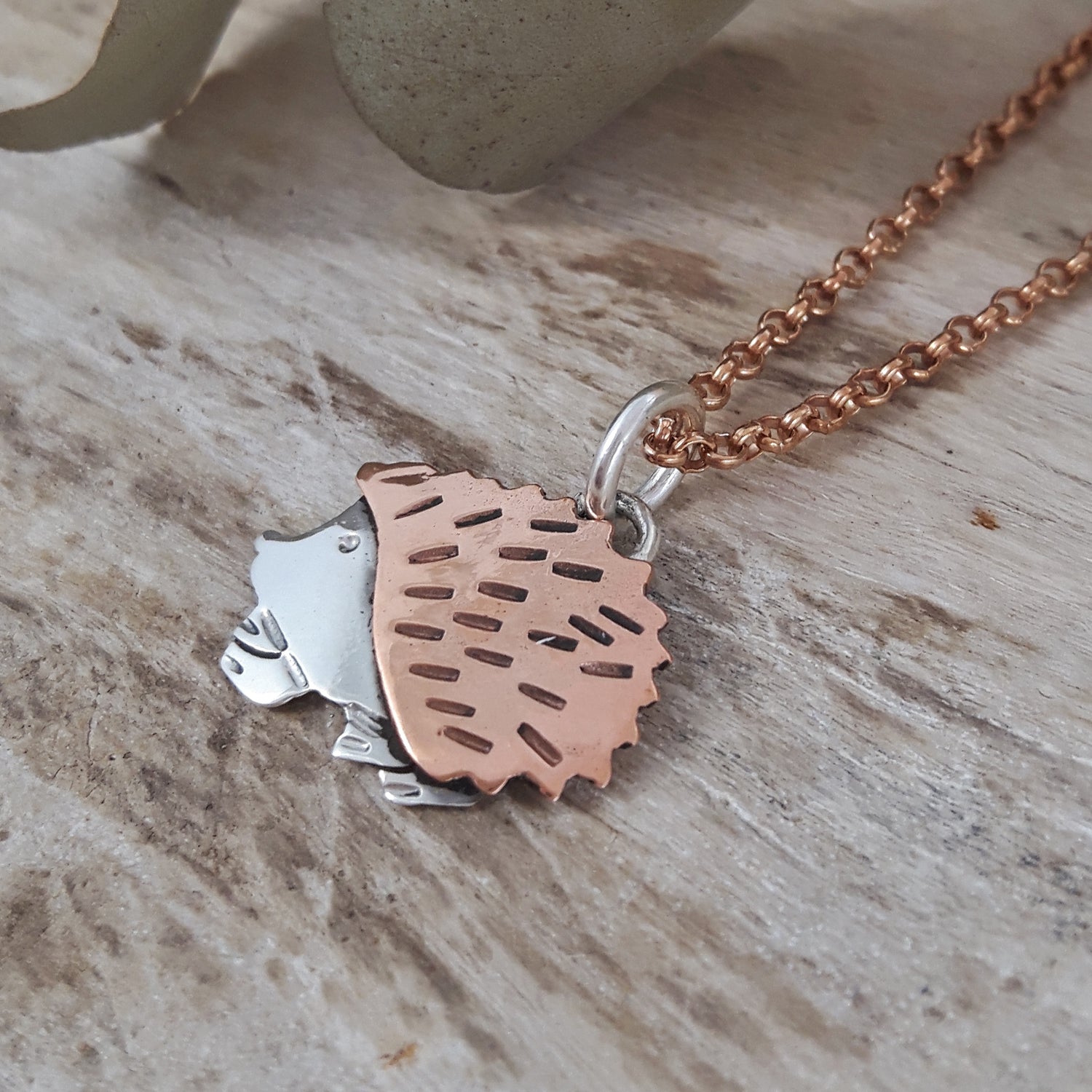 Copper and sterling silver hedgehog pendant  with a rose gold chain on a wooden surface