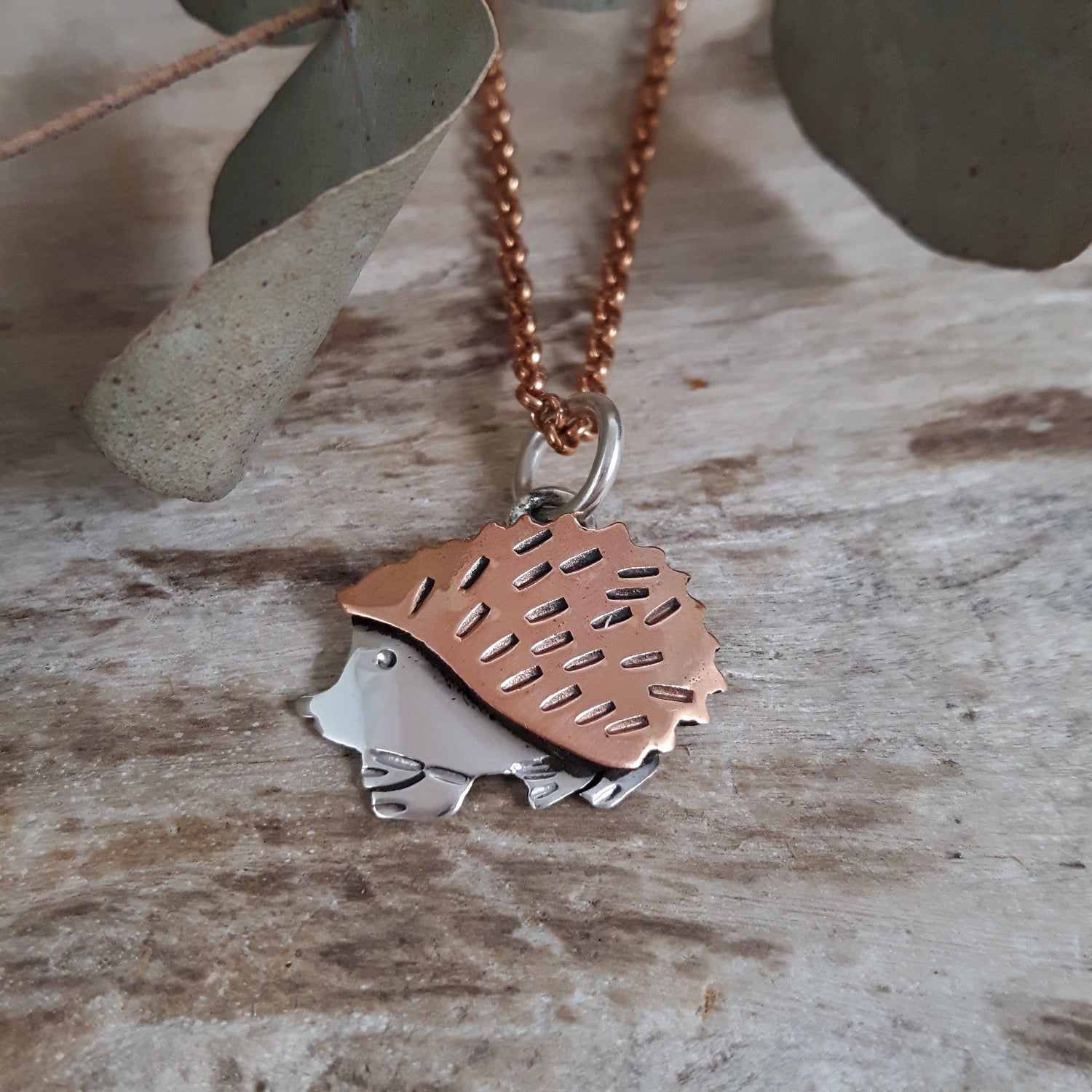 Copper and sterling silver hedgehog pendant on a rose gold chain against a natural background