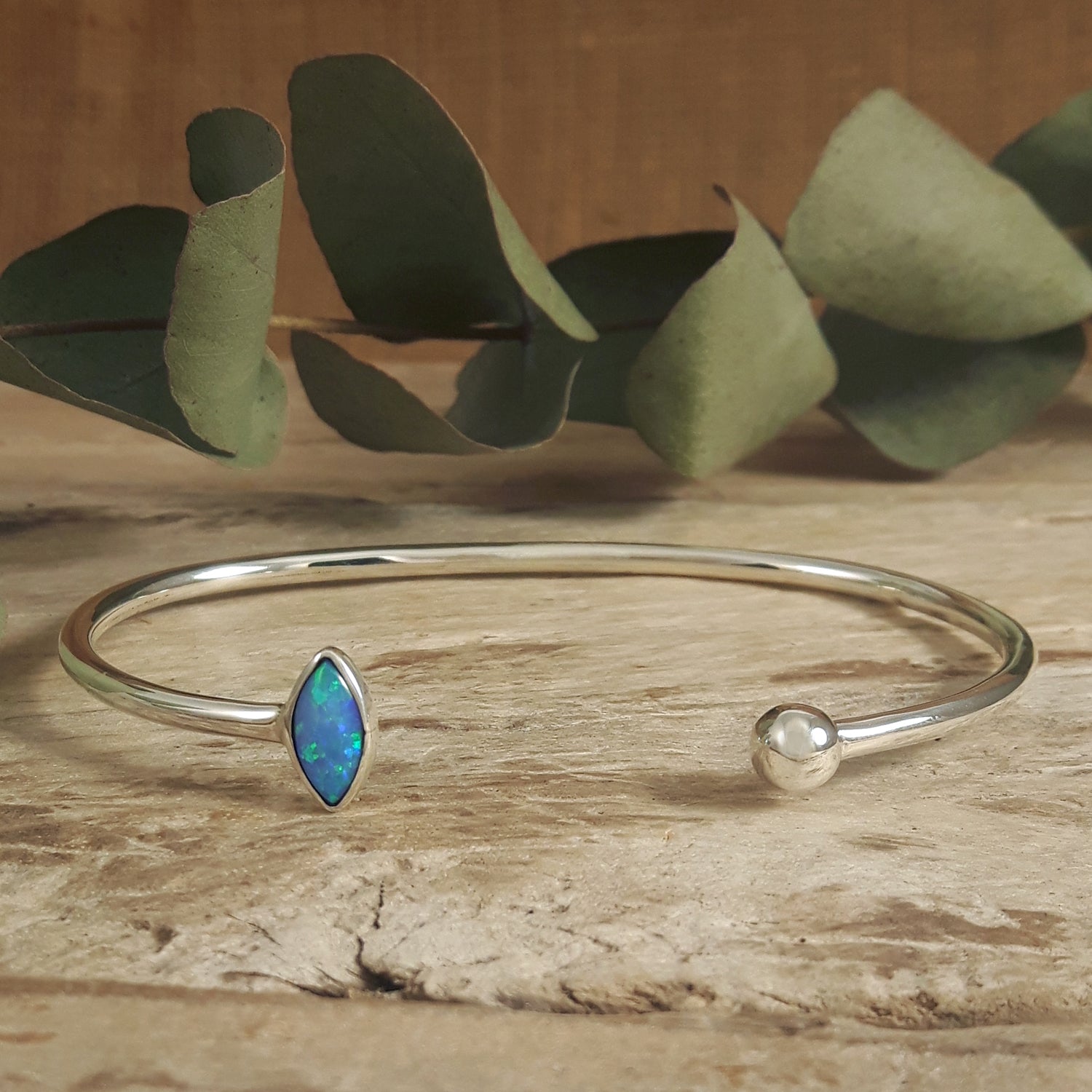 Silver bracelet with an opalite stone on a wooden surface with eucalyptus leaves.