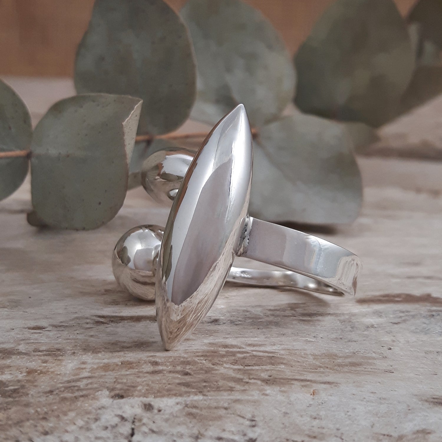 Maya polished sterling silver ring with a unique design on a wooden surface with eucalyptus leaves in the background