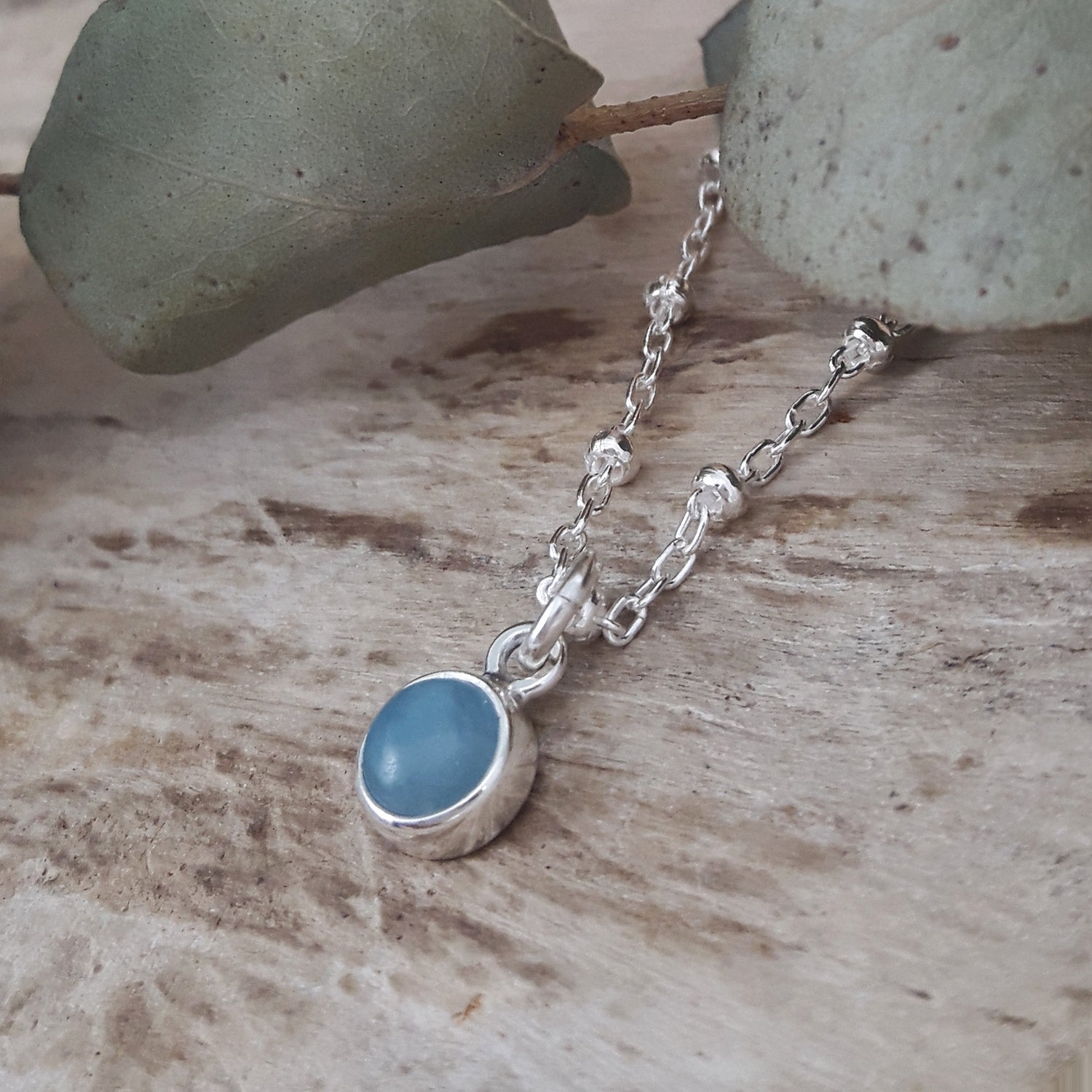 Silver chain necklace with an aquamarine pendant on a wooden surface