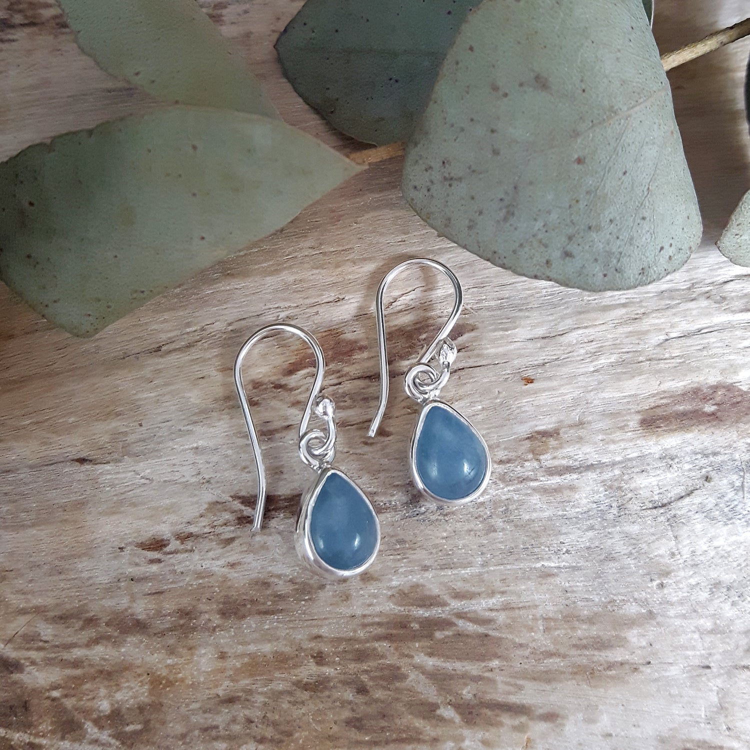 Silver earrings with aquamarine teardrop stones on a wooden surface