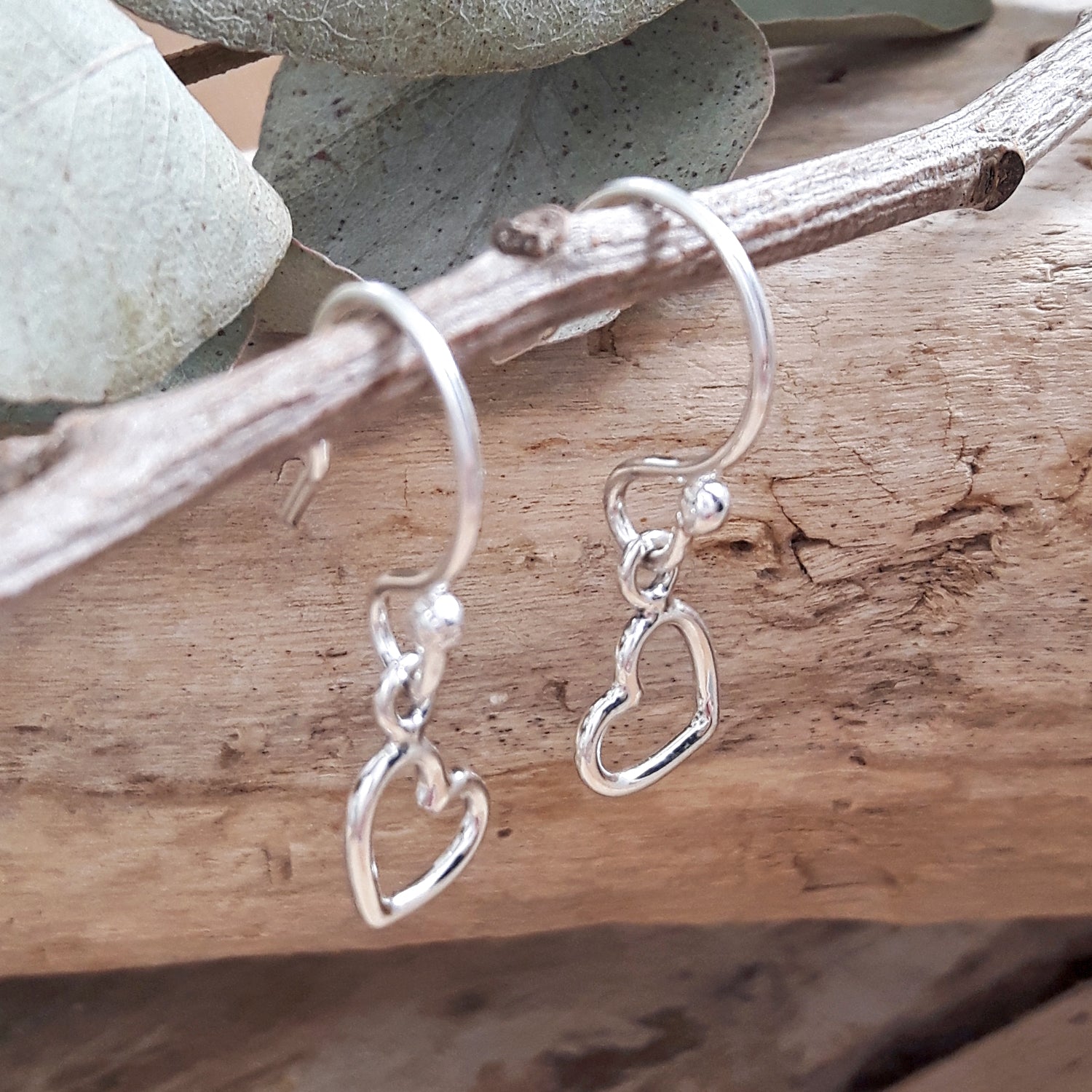 Sterling silver open heart-shaped earrings on a wooden branch with a natural background, designed in England