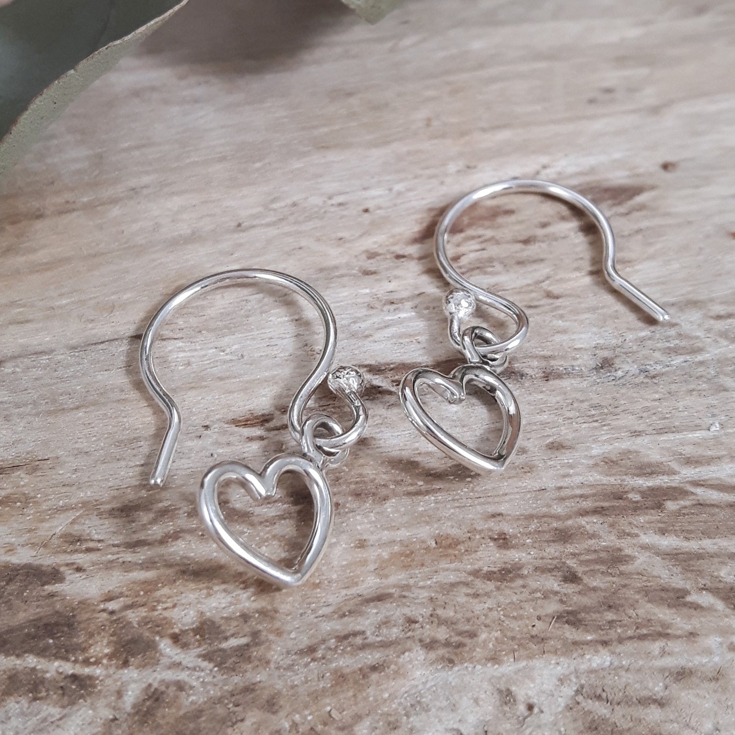 Minimalist sterling silver open heart-shaped earrings on a wooden surface