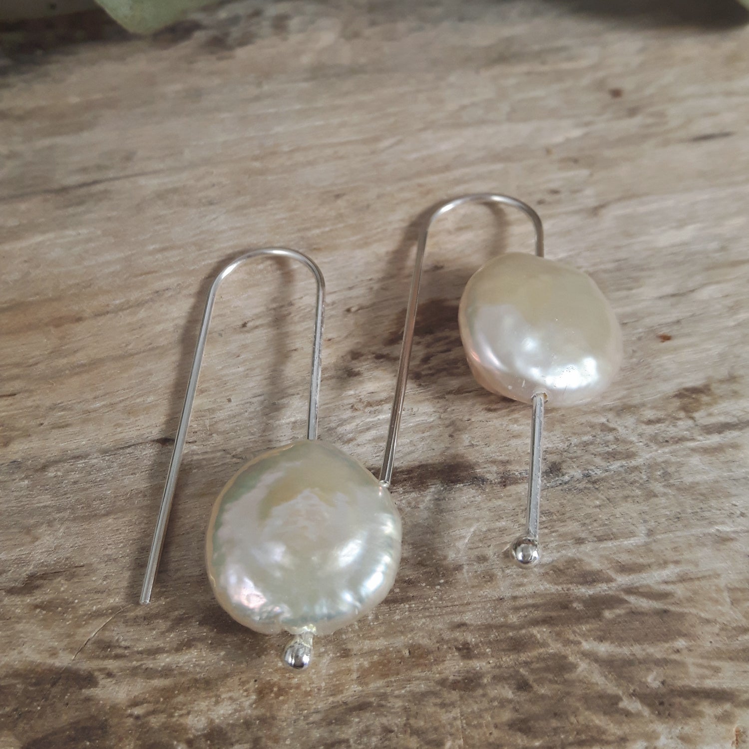 Pair of white baroque pearl earrings on a wooden surface