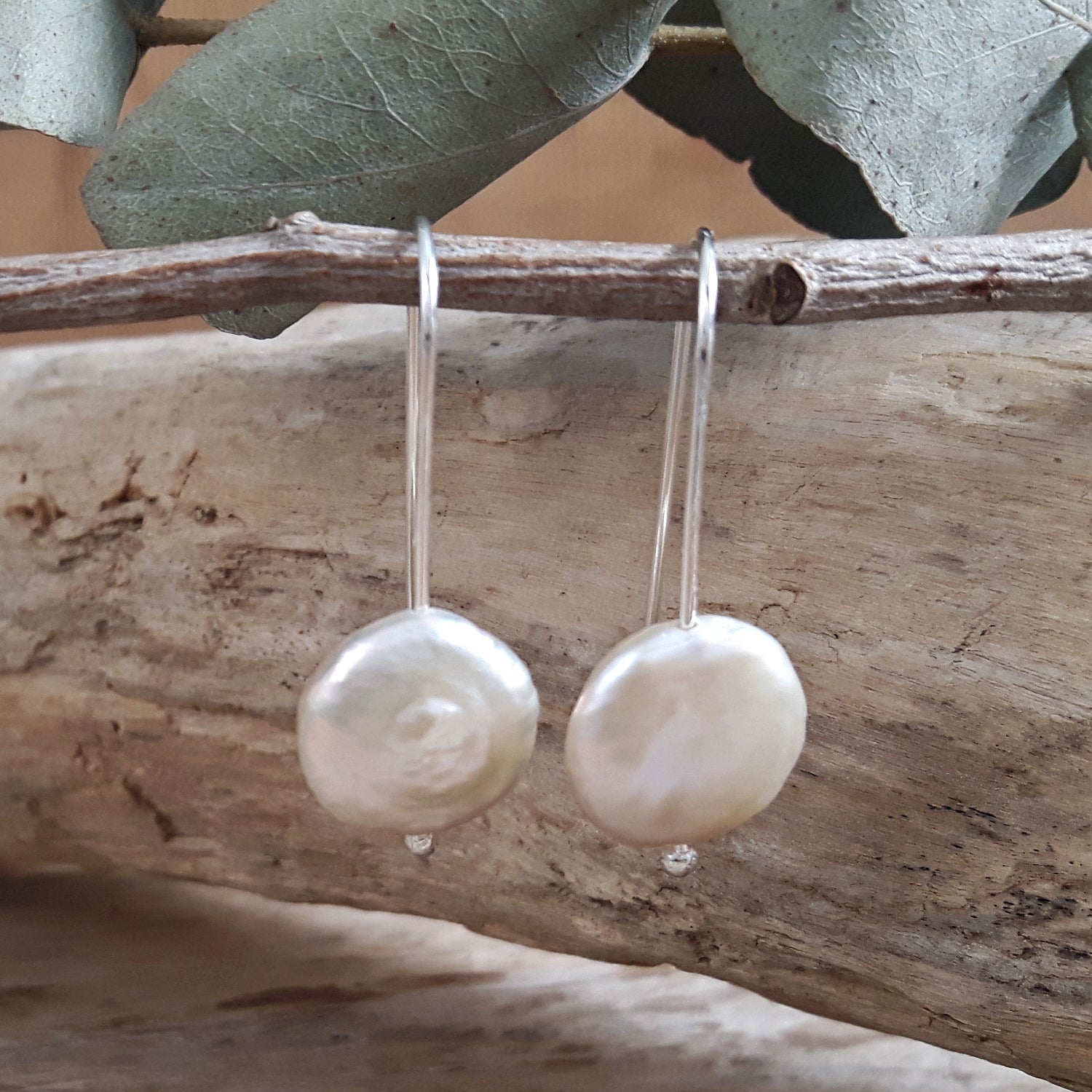 Pearl earrings hanging from a branch with natural background