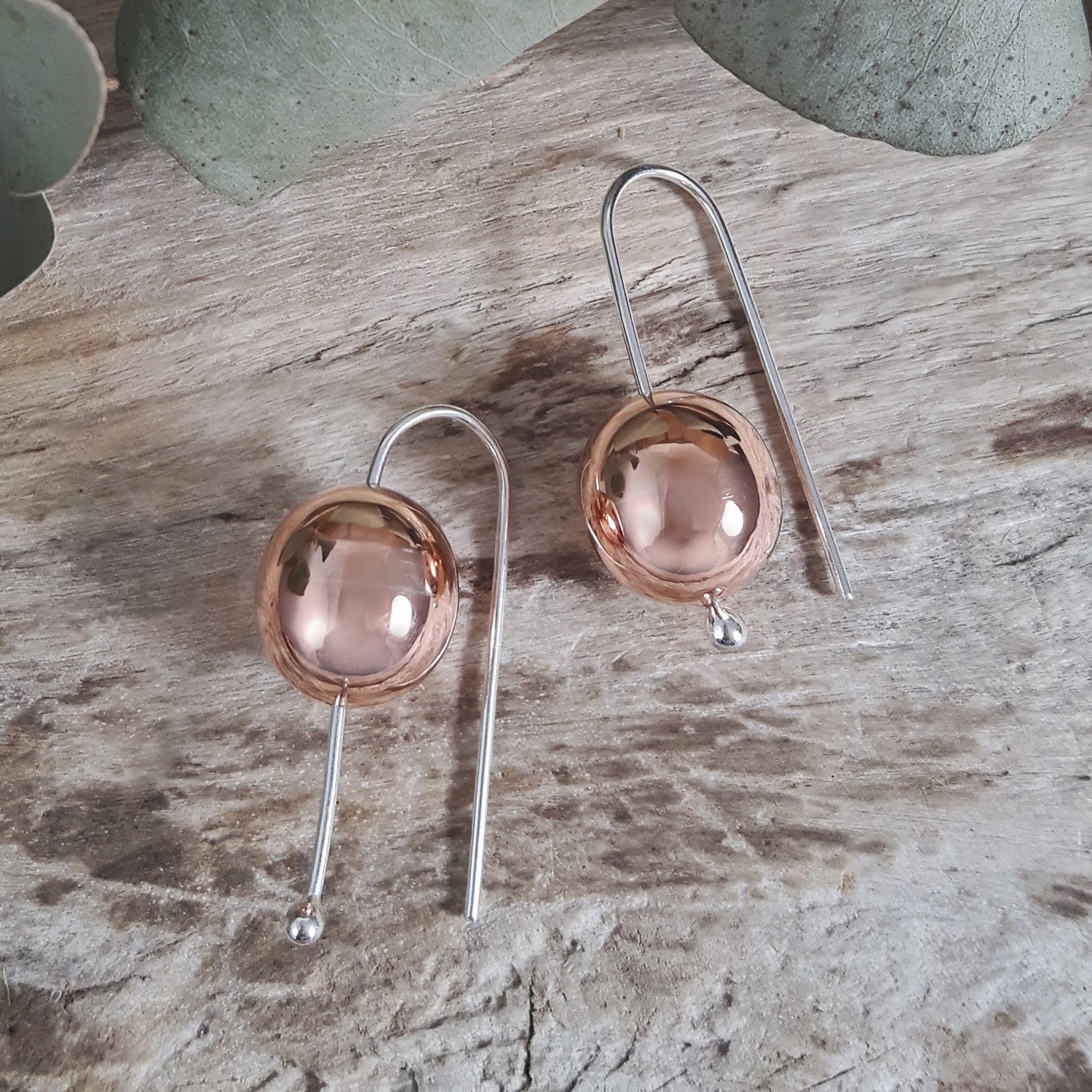 Pair of copper and silver earrings on a wooden surface
