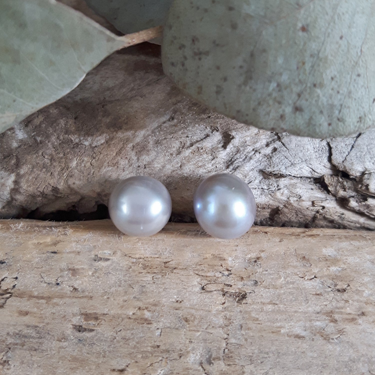 Two pearl earrings on a natural wooden surface with leaves in the background