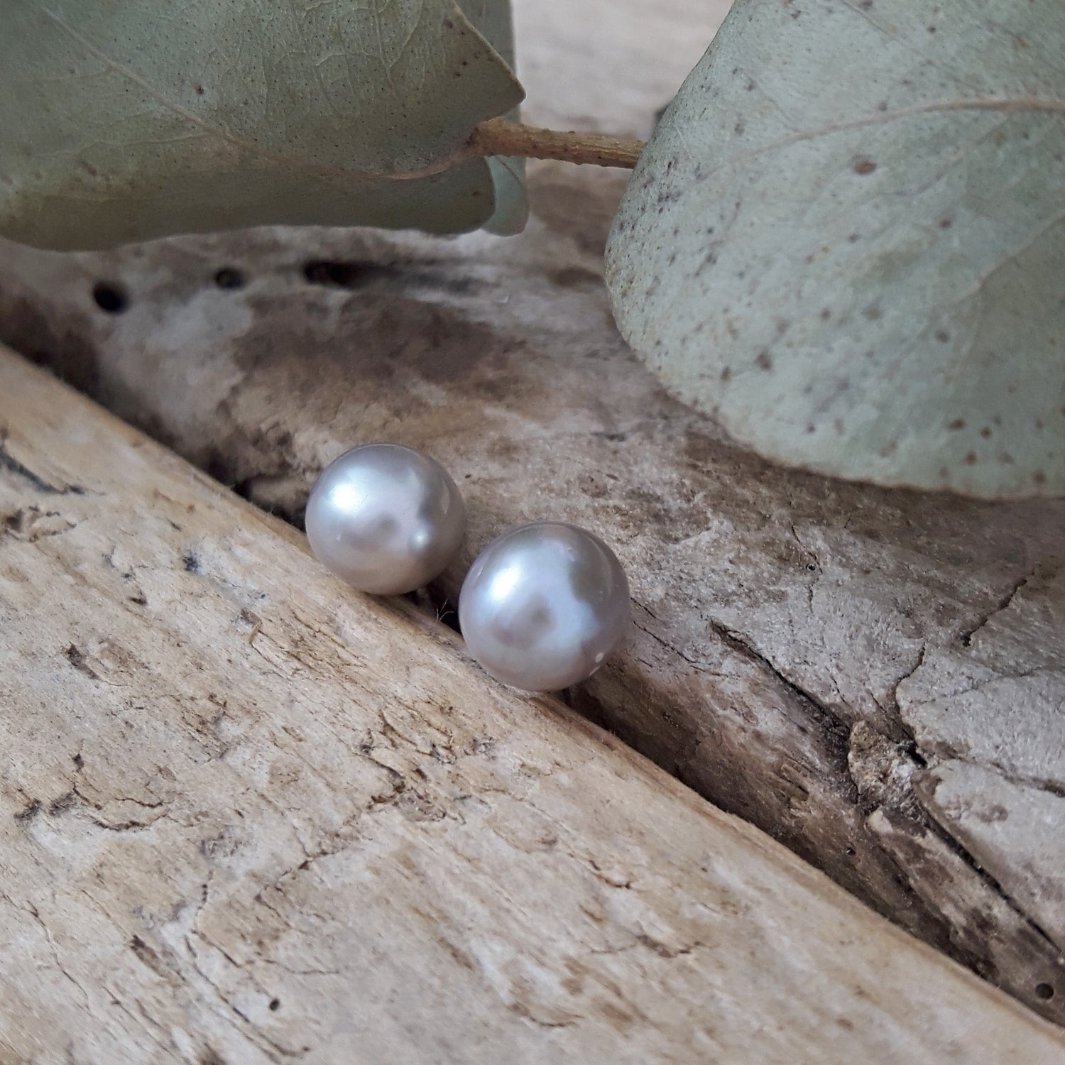 Pearl earrings on a wooden surface with leaves in the background