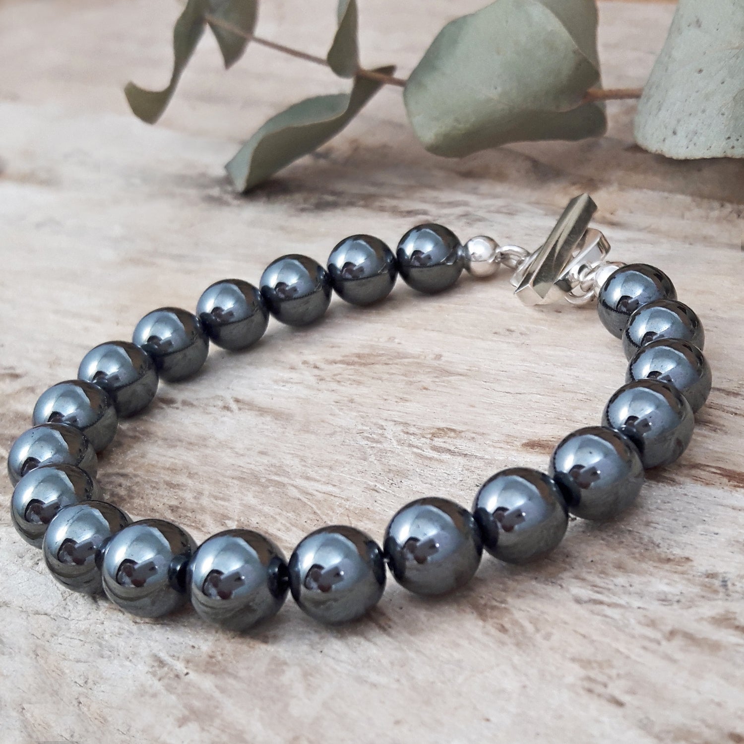 Hematite beaded bracelet on a wooden surface with green leaves in the background
