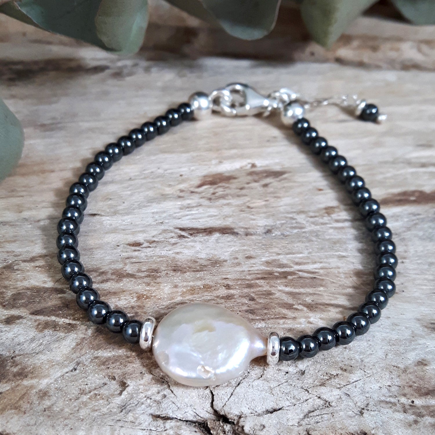 Hematite gemstone beaded bracelet with a large white pearl on a wooden surface, artisan jewellery UK