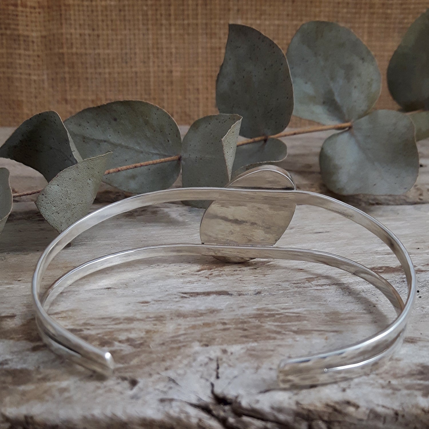 Sterling silver cuff bracelet on a wooden surface with eucalyptus leaves in the background