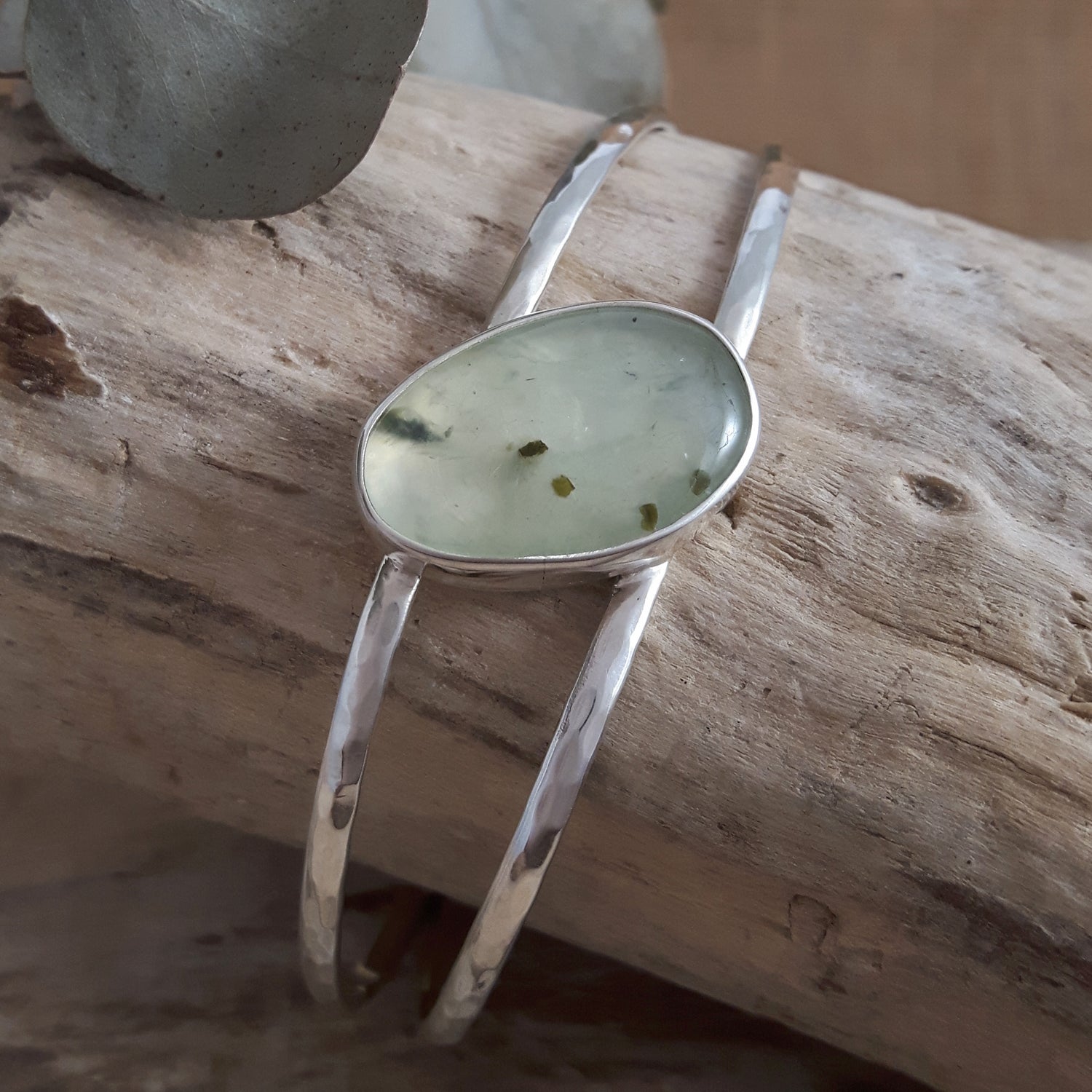 Sterling silver cuff bracelet with a green prehnite stone on a wooden surface
