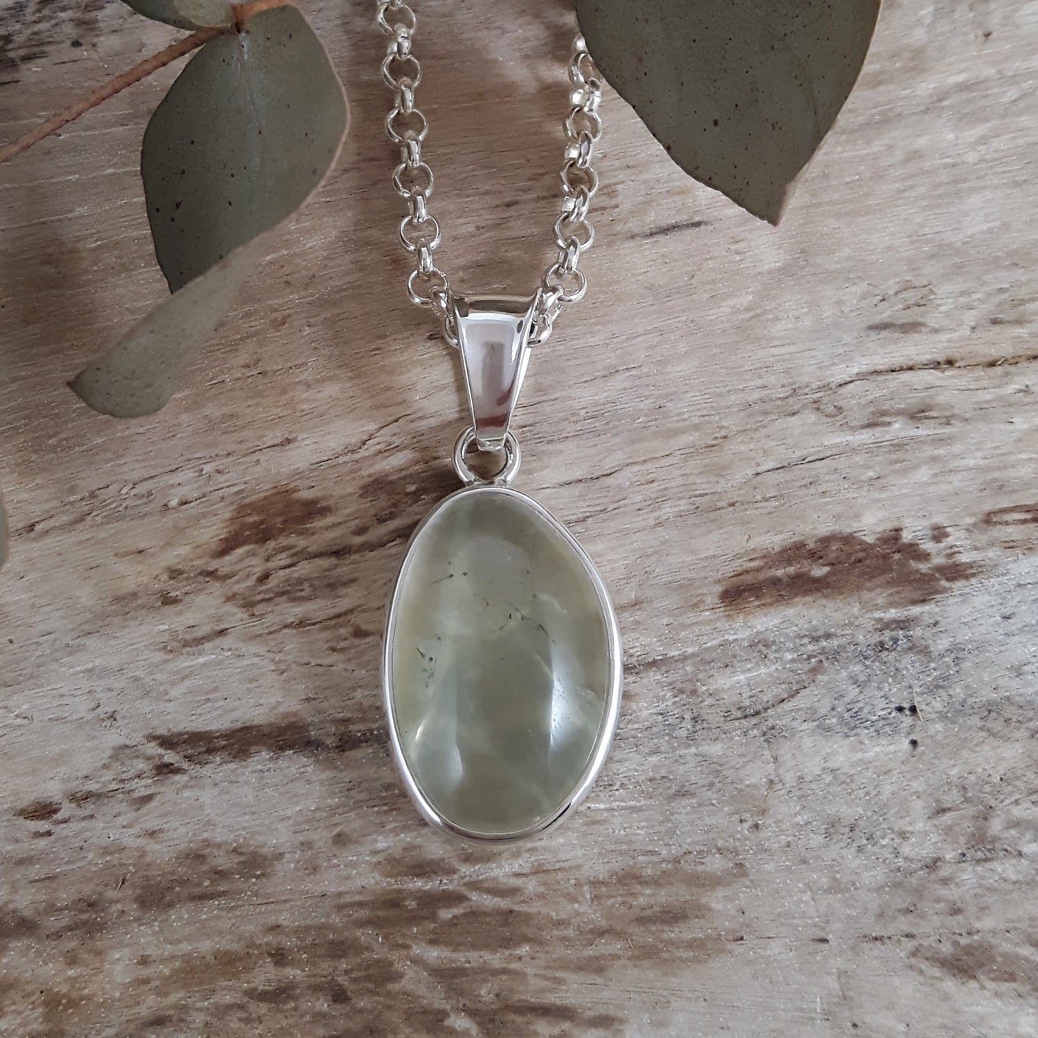 Sterling silver pendant with a green prehnite stone with a silver chain on a wooden surface