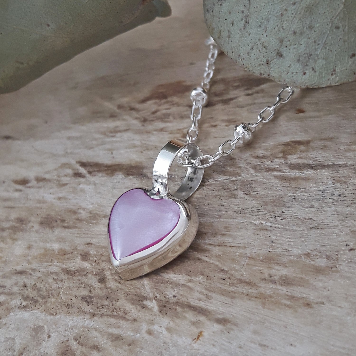 Sterling silver chain necklace with a heart-shaped pink mother-of-pearl pendant on a wooden surface