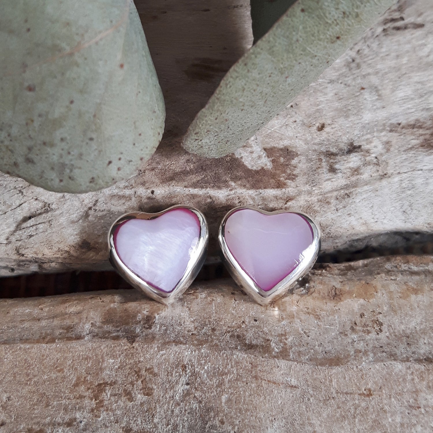 Heart-shaped pink mother-of-pearl earrings with silver frame on a wooden surface