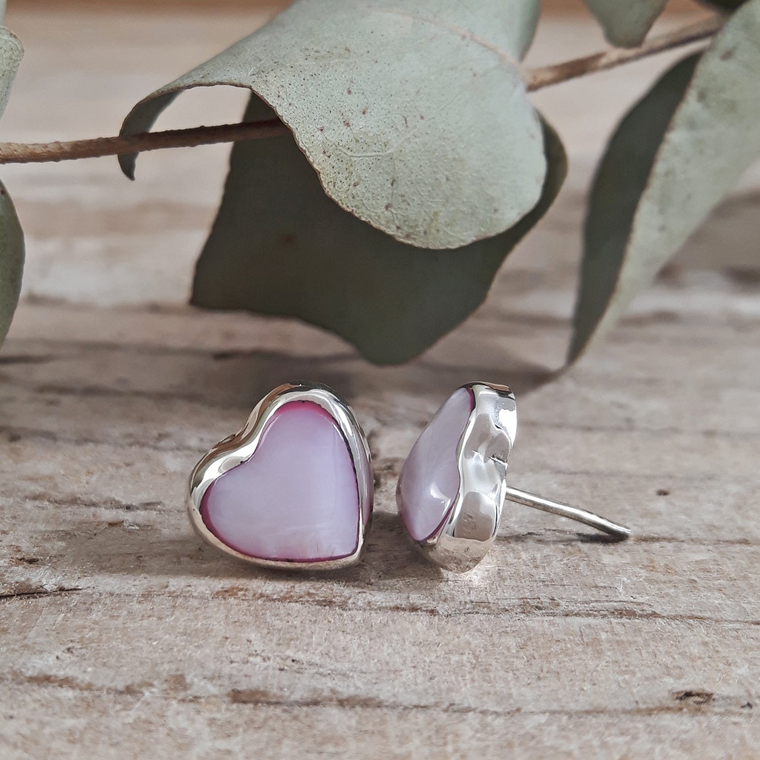 Heart-shaped earrings on a wooden surface with leaves in the background