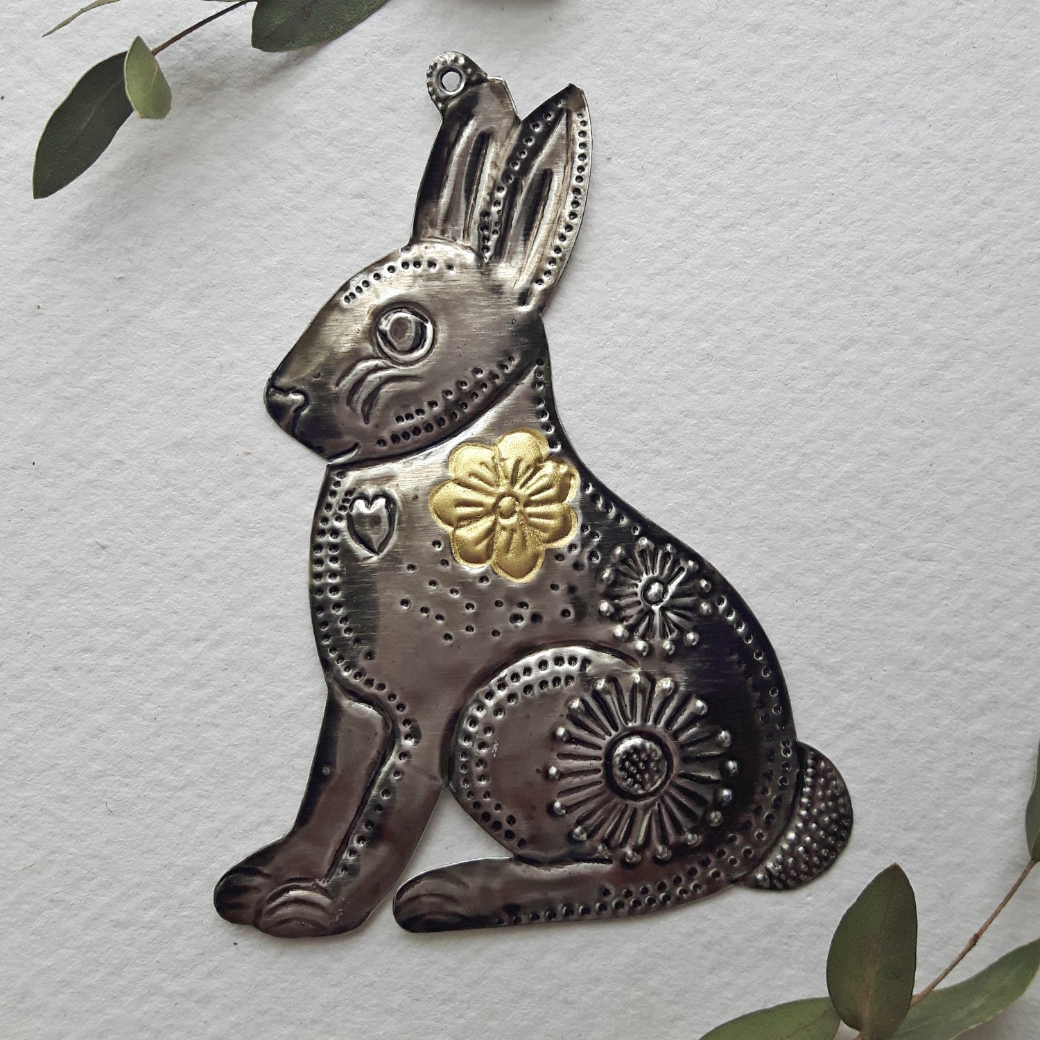 Decorative metal rabbit wall art on a light gray background with green leaves.