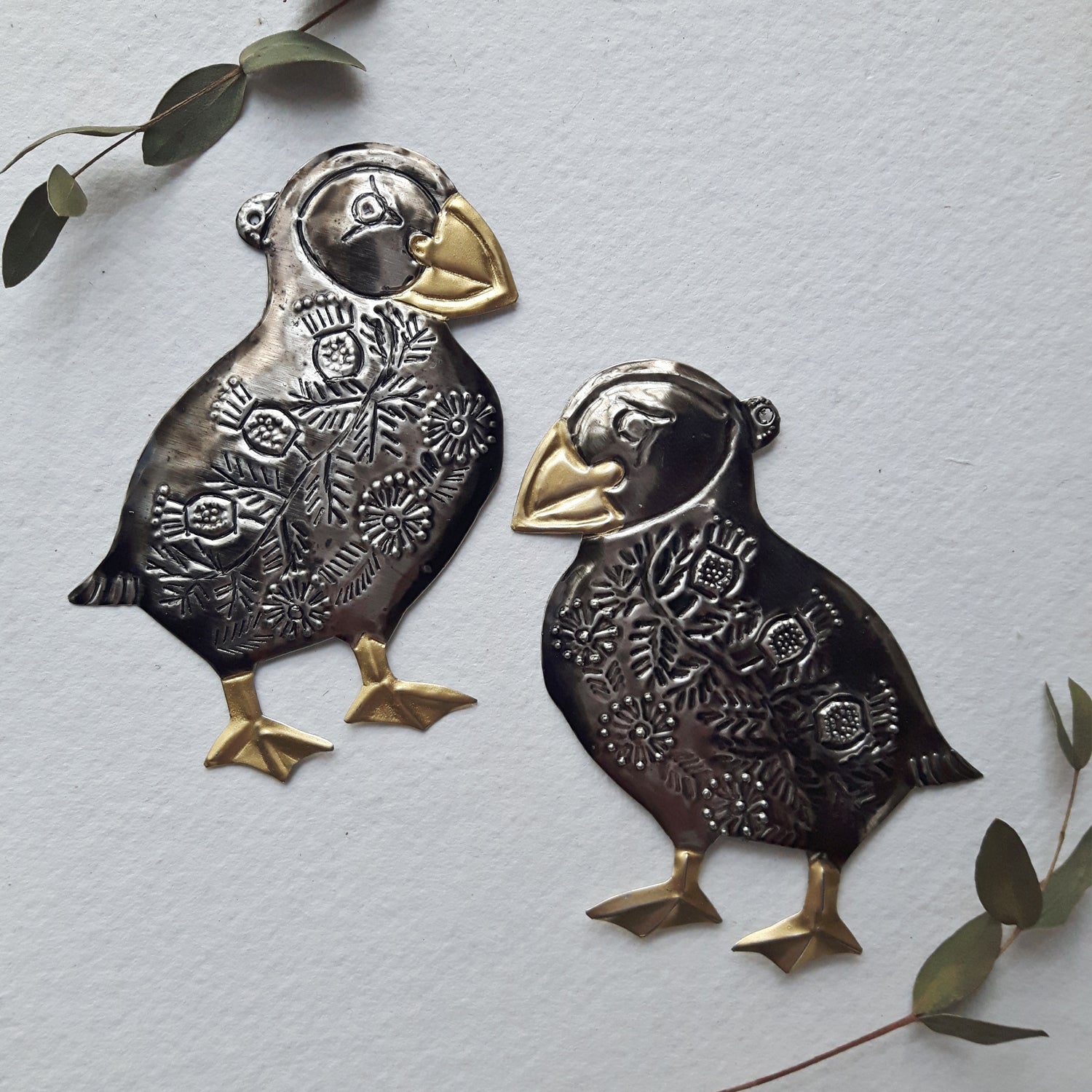 Two decorative metal puffins on a light gray background with green leaves.
