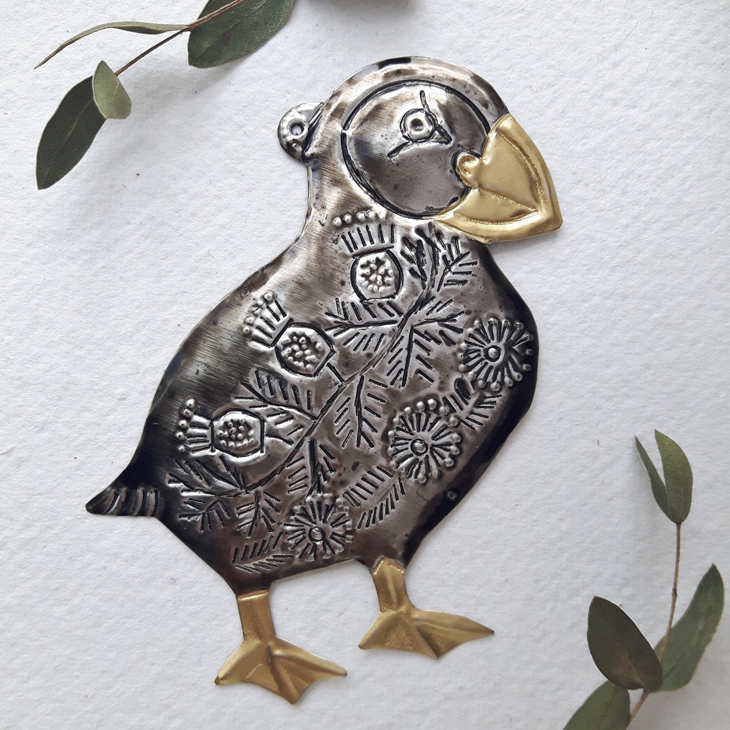 Decorative metal puffin ornament with floral patterns on a white background