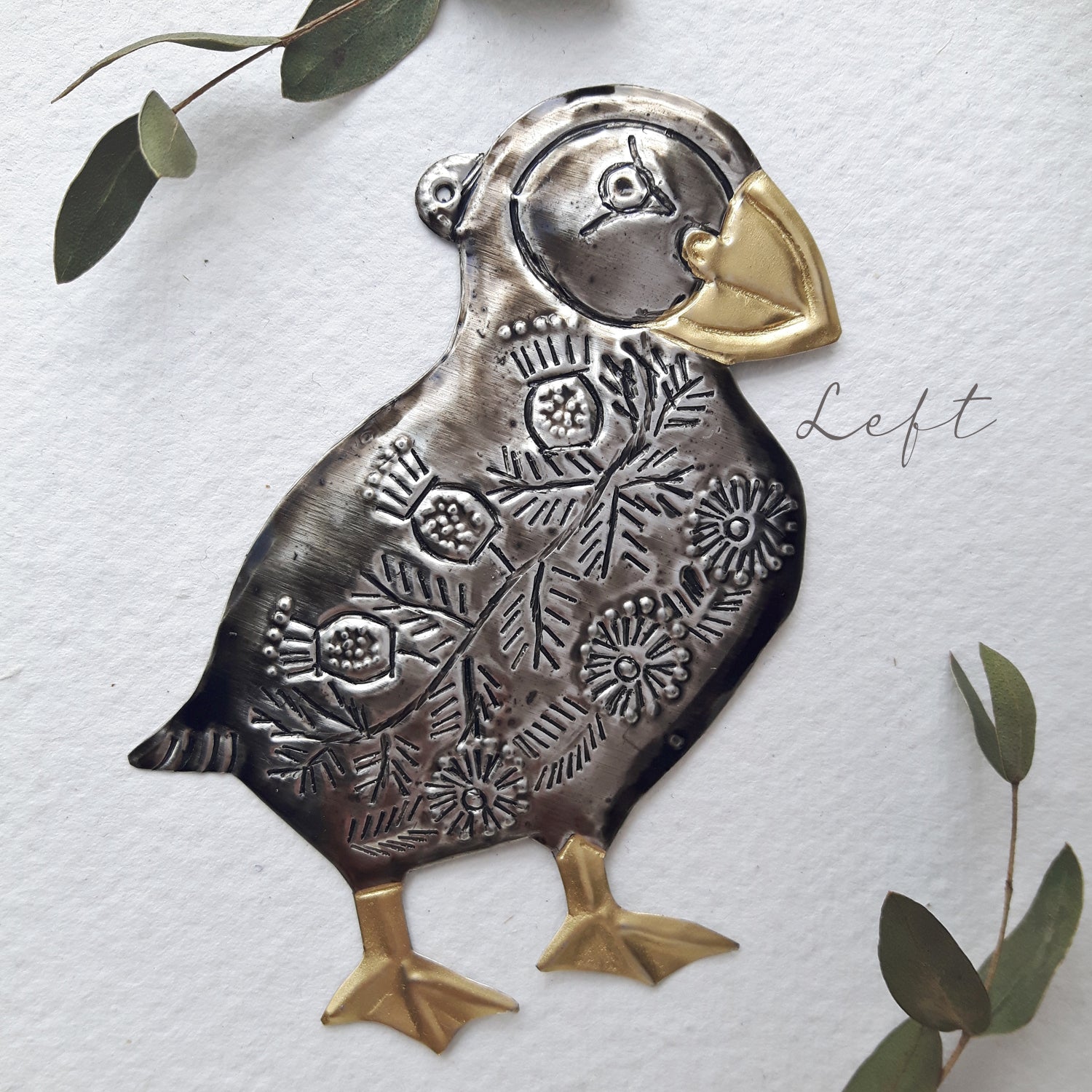 Decorative metal puffin ornament with floral patterns on a white background