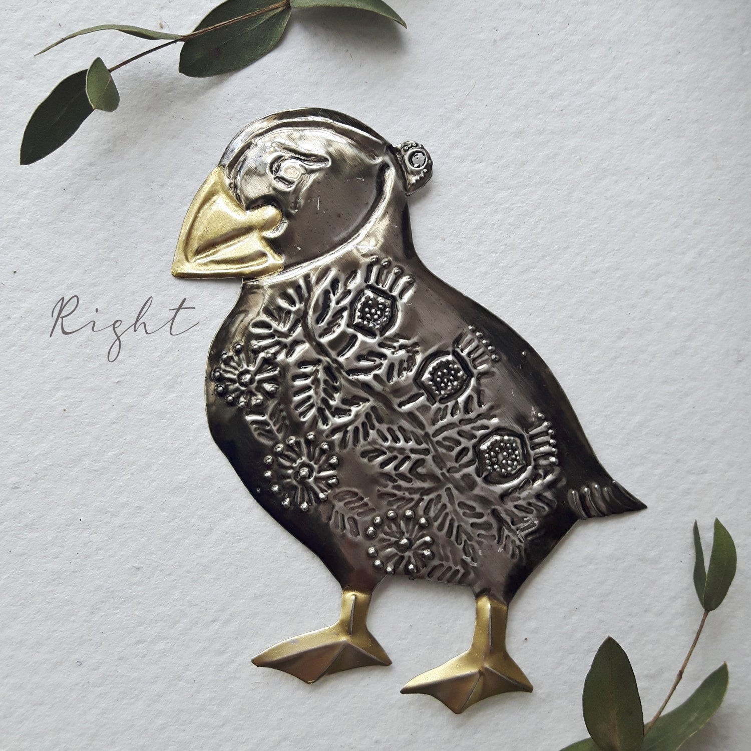 Decorative metal puffin ornament with gold accents on a light gray background