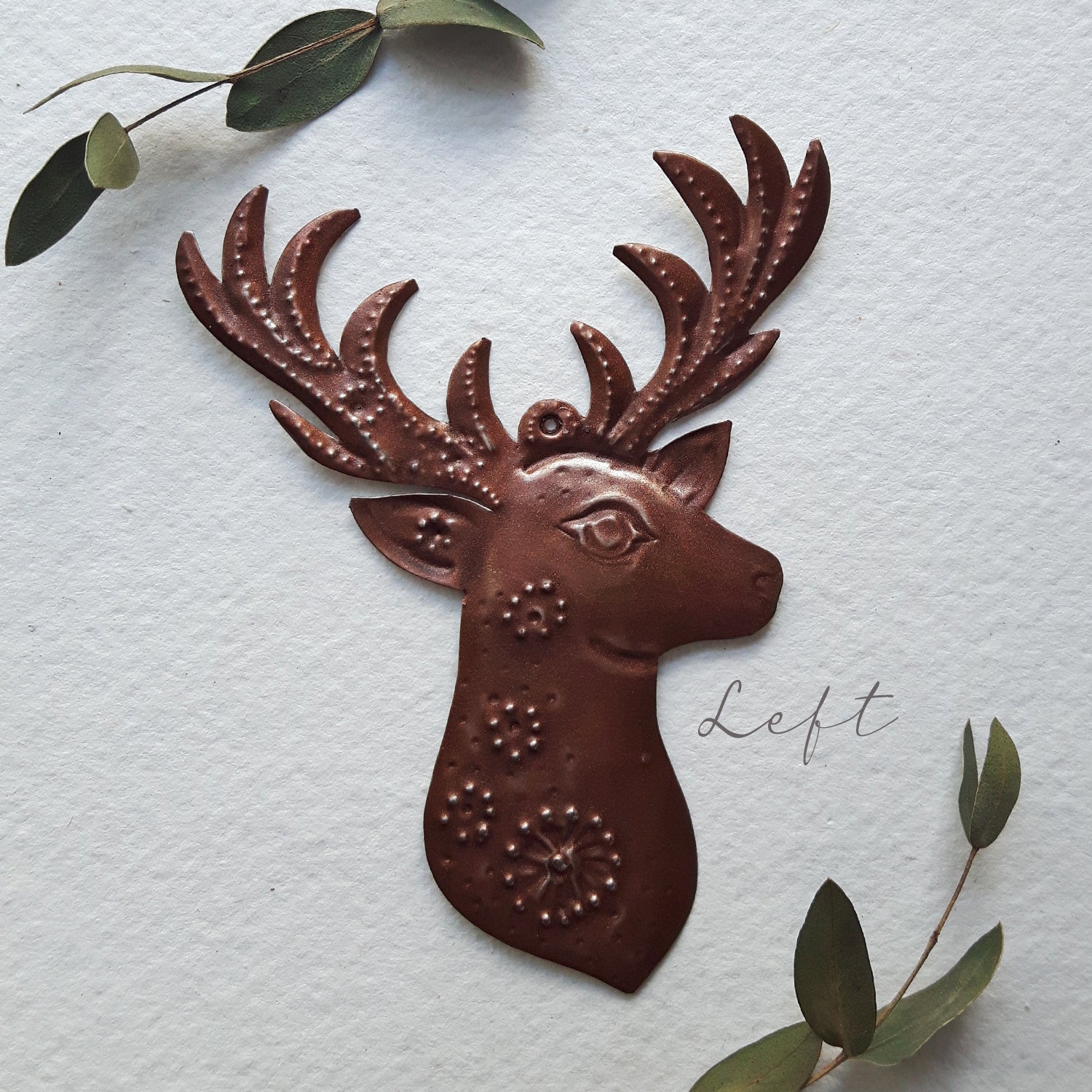 Decorative metal deer head wall art on a textured white background with green leaves.