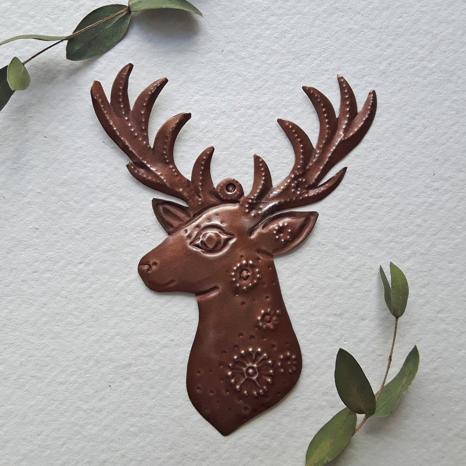 Decorative metal deer head wall art on a textured light gray background with green leaves.