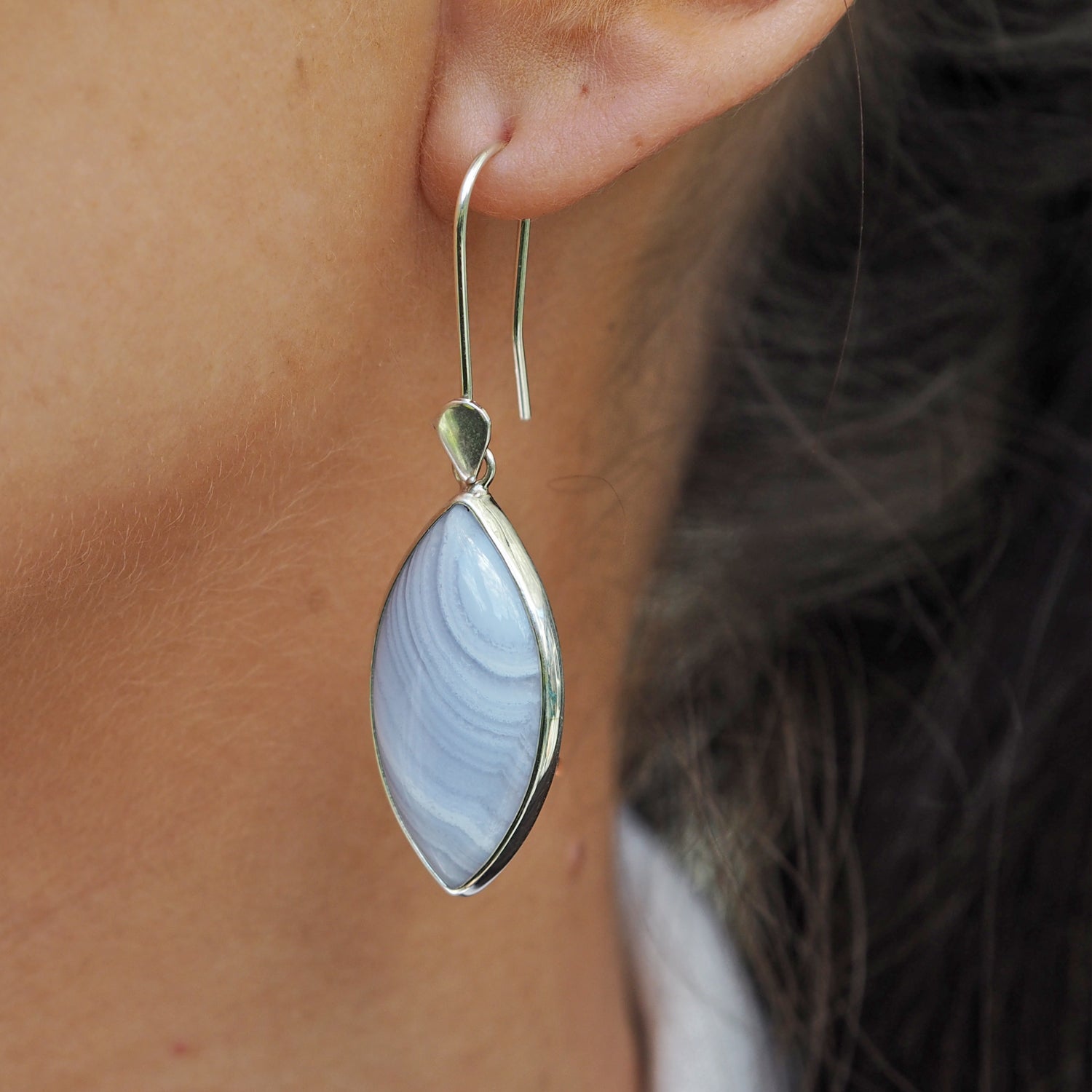 Unique blue lace agate gemstone earrings with sterling silver detail worn in an ear