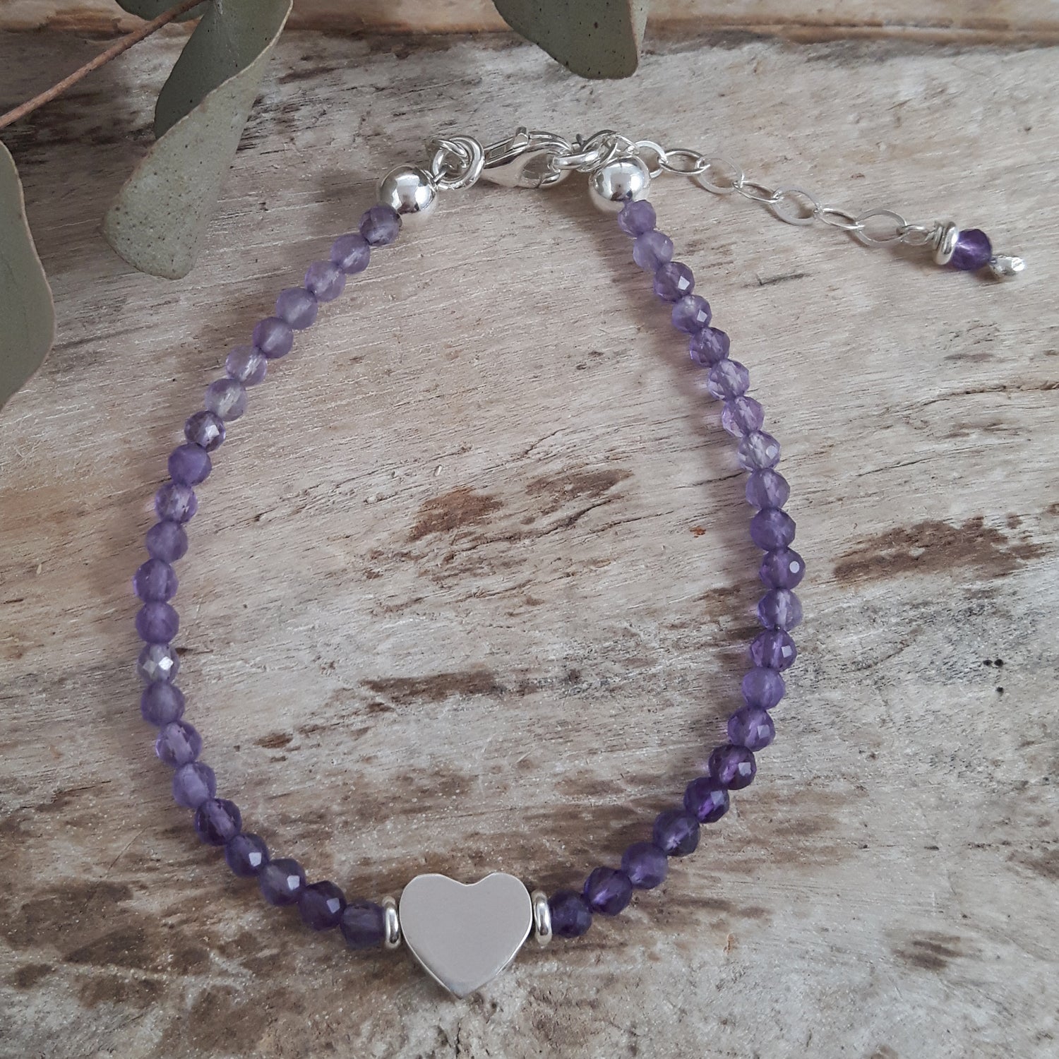 Amethyst beaded bracelet with a silver heart charm on a wooden surface