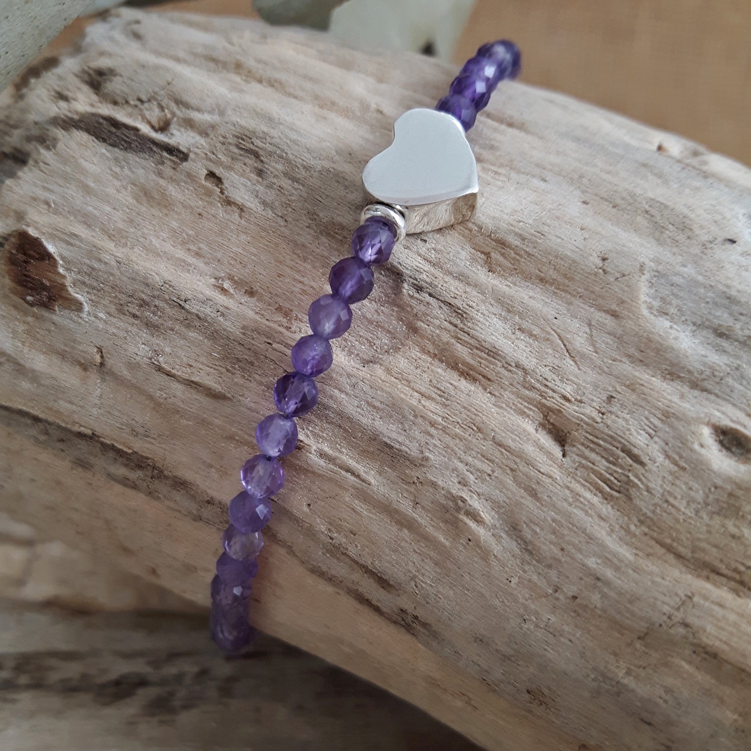 Amethyst beaded bracelet with a silver heart charm on a wooden surface