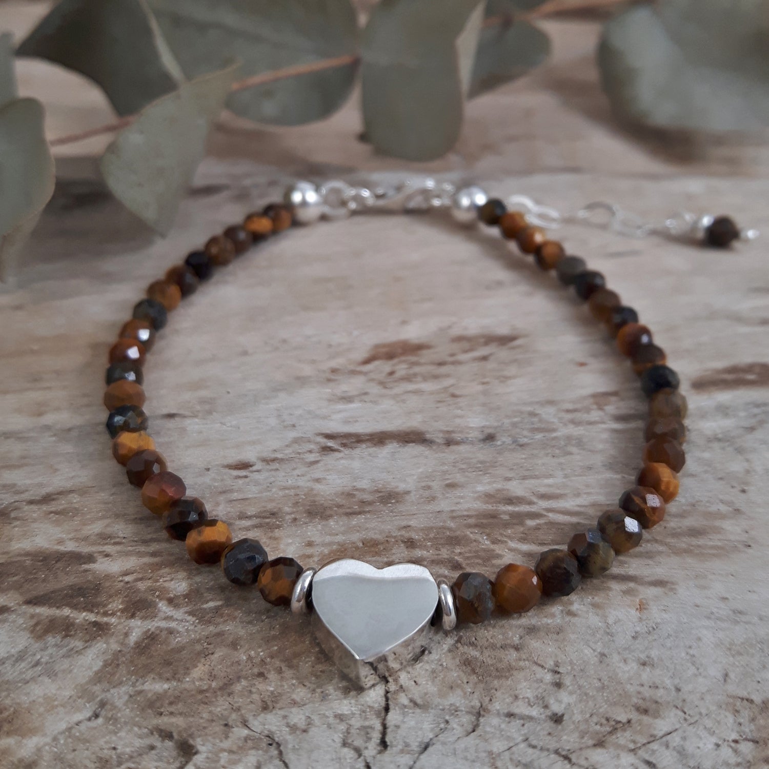 Tiger's Eye beaded birthstone bracelet with a sterling silver heart charm on a textured surface