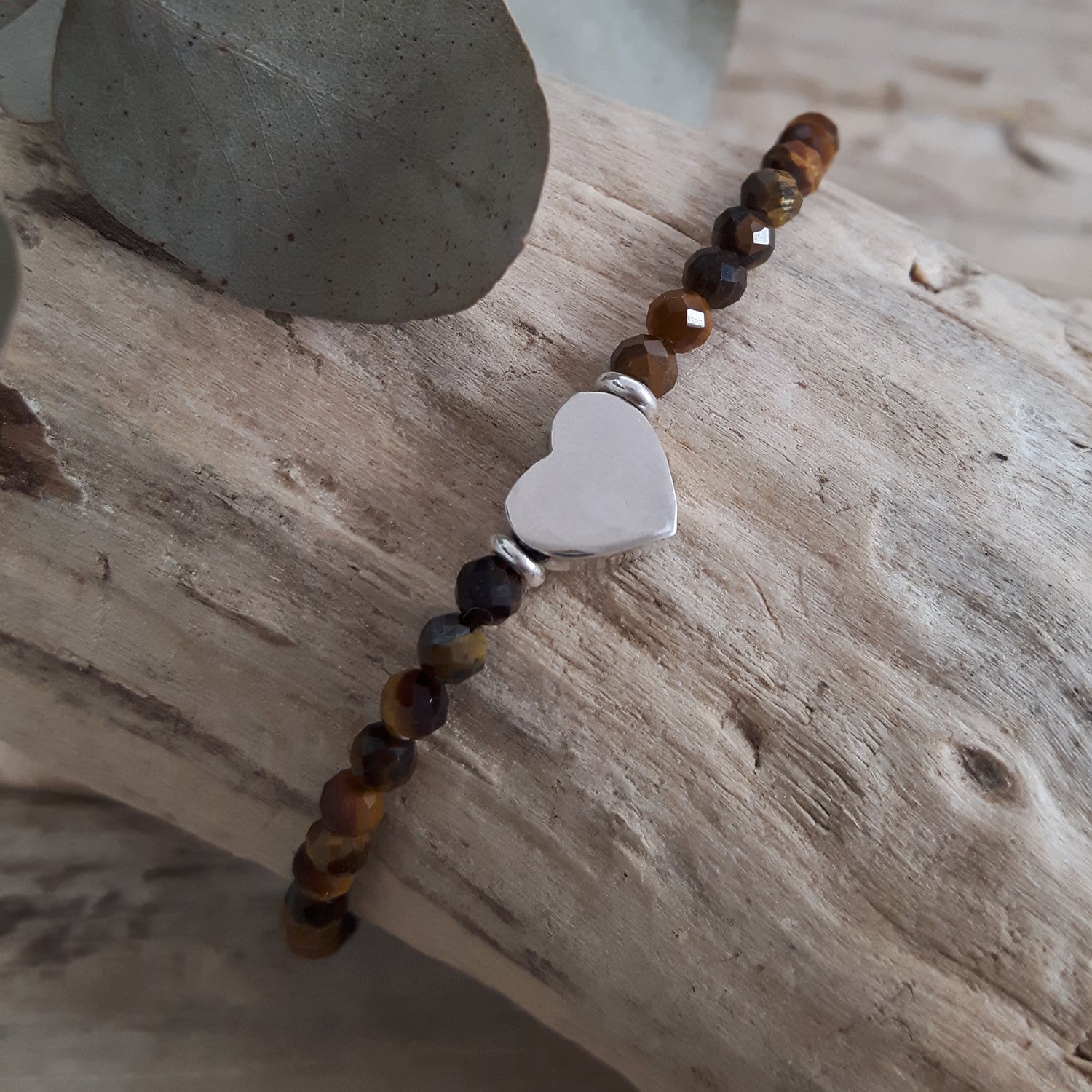 Tiger's Eye beaded bracelet with a sterling silver heart-shaped charm on a wooden surface